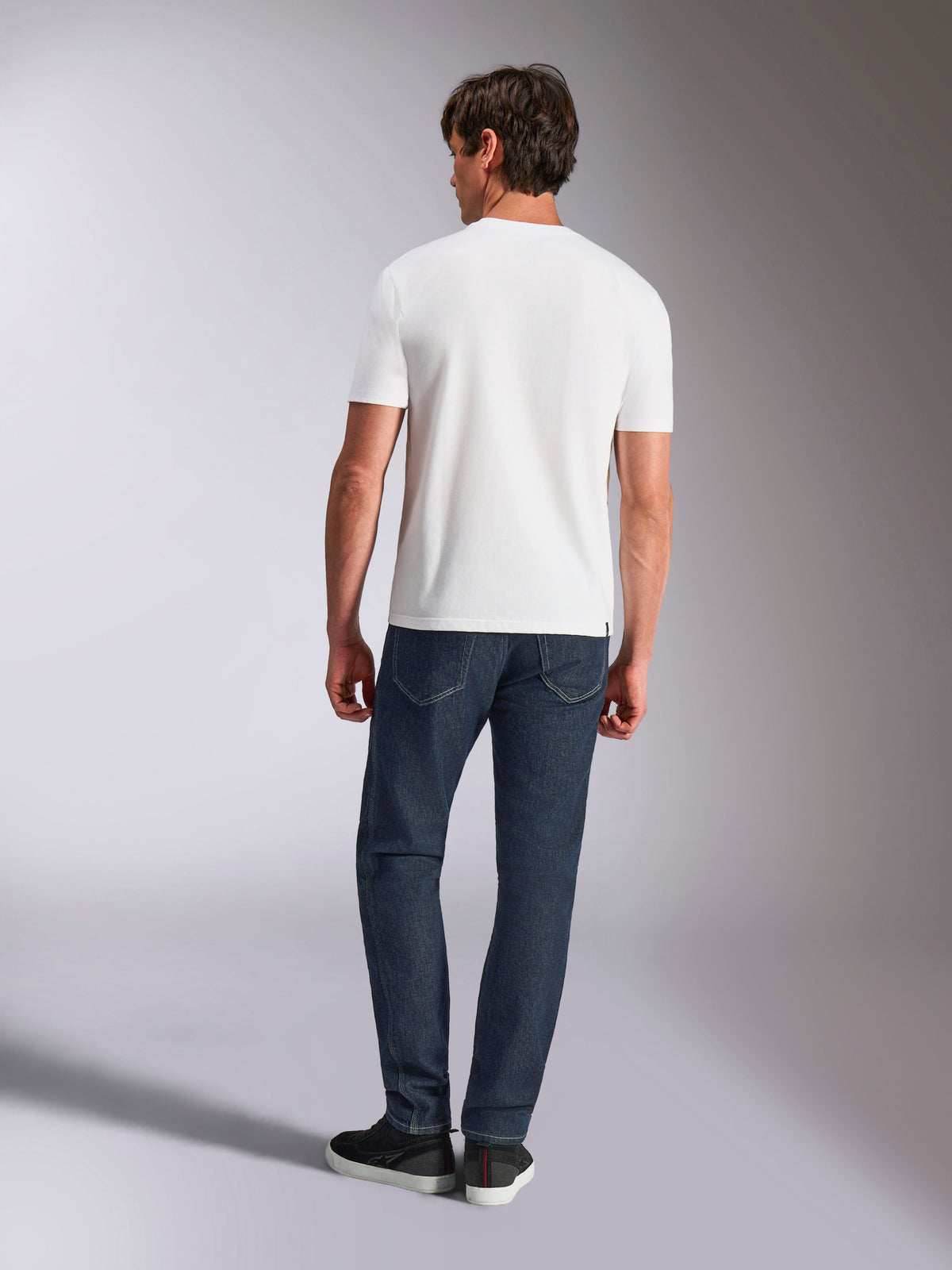 Alpinestars Abus CSF Tee, koszulka z krótkim rękawem, biała, widok z tyłu na modela ubranego w białą koszulkę i ciemne jeansy, codzienna odzież uliczna inspirowana motorsportem