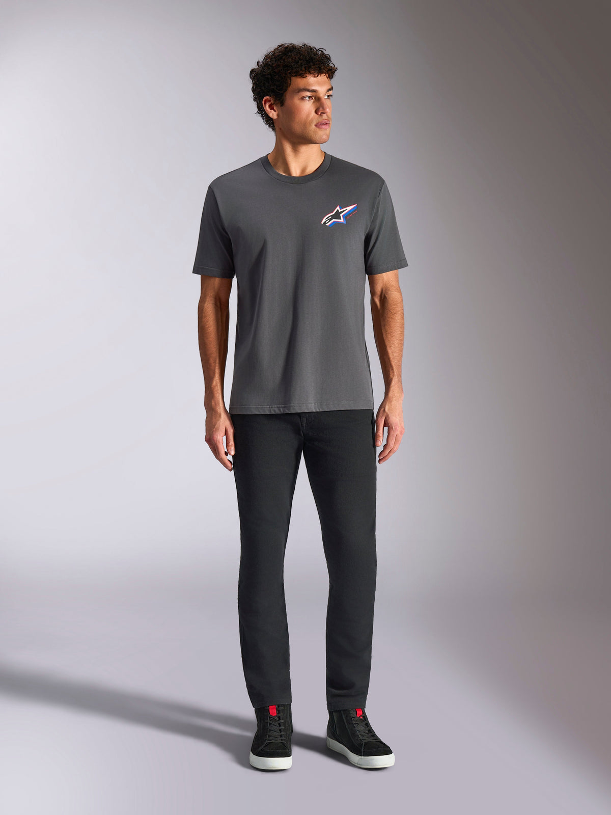 Alpinestars Angler CSF Tee, Short Sleeve T-Shirt, Charcoal, featuring a vibrant multi-color Astars logo on the chest, worn by a model with black pants and sneakers, Casual Motorsport Streetwear