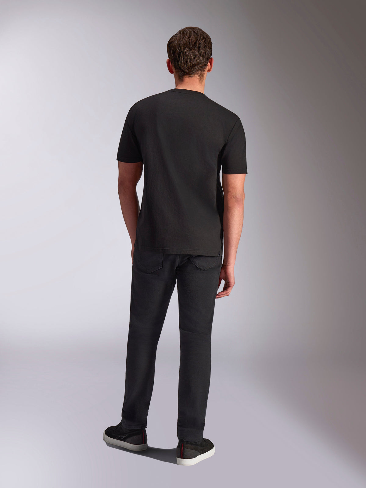 Alpinestars Trifecta CSF Tee, koszulka z krótkim rękawem, czarna, widok z tyłu na modelu, zestawiona z czarnymi spodniami i czarnymi sneakersami, codzienna odzież uliczna inspirowana motorsportem