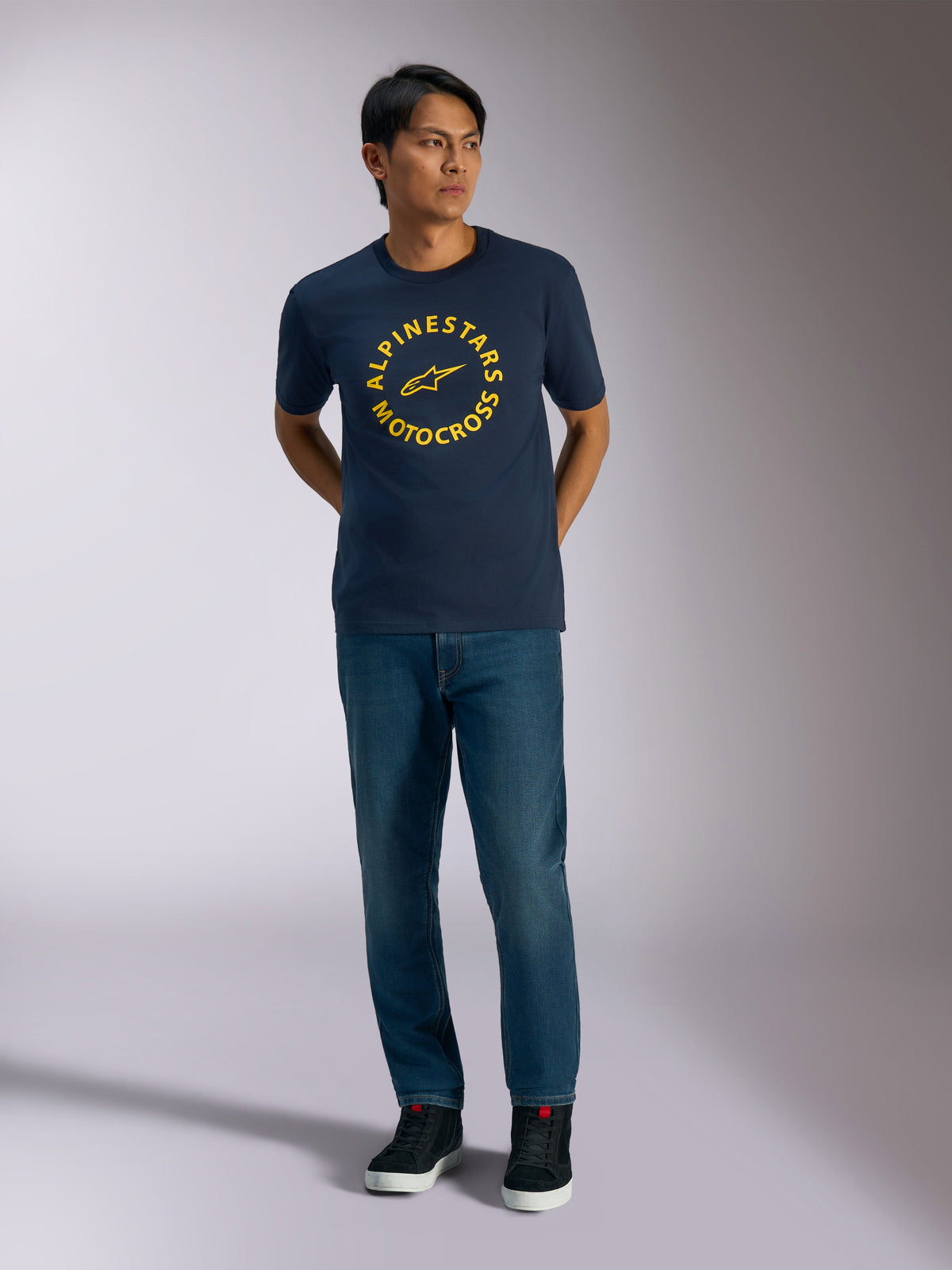 Alpinestars MX CSF Tee, Short Sleeve T-Shirt, Navy Blue, featuring a yellow circular Alpinestars Motocross graphic, worn by a model with blue jeans and black sneakers, casual motorsport streetwear