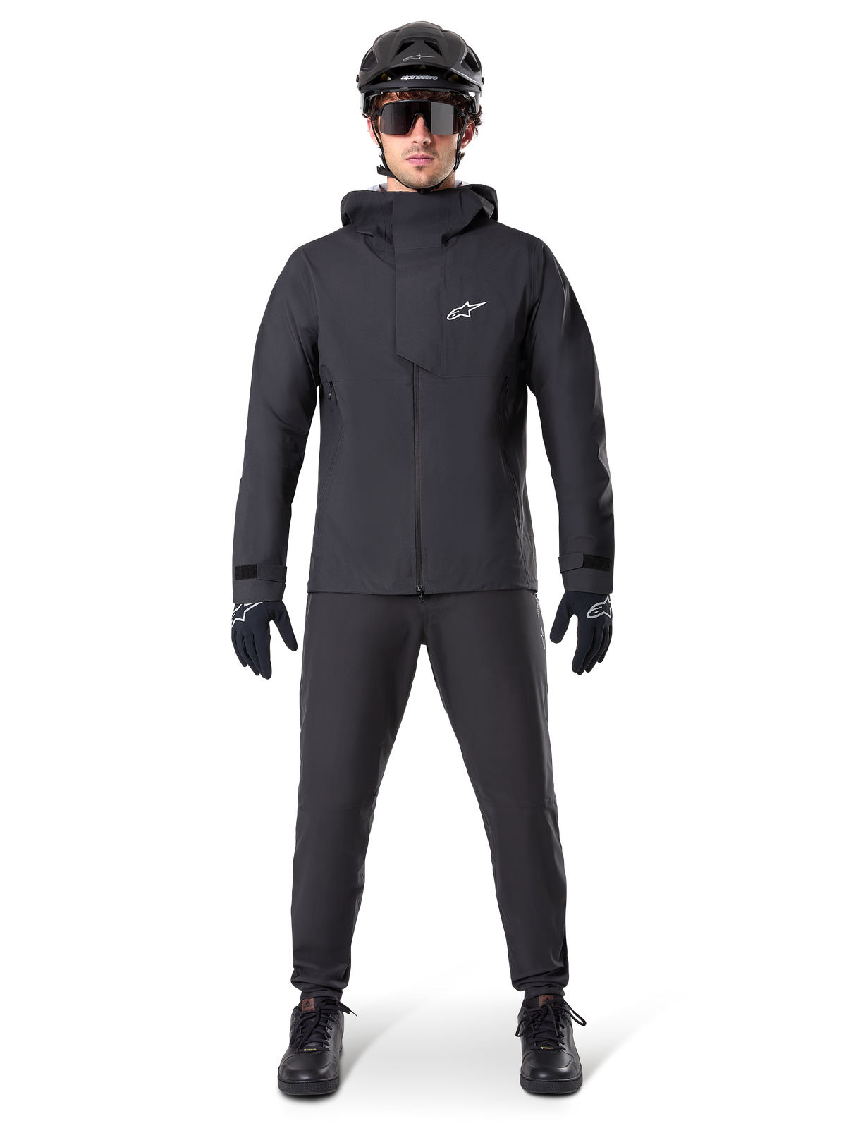 Alpinestars A-Dura Elite Waterproof Jacket, czarna, noszona z pasującymi spodniami rowerowymi i rękawiczkami, czarny kask i okulary przeciwsłoneczne, z białym logo Astars na piersi, wysokowydajna techniczna konstrukcja do kolarstwa górskiego