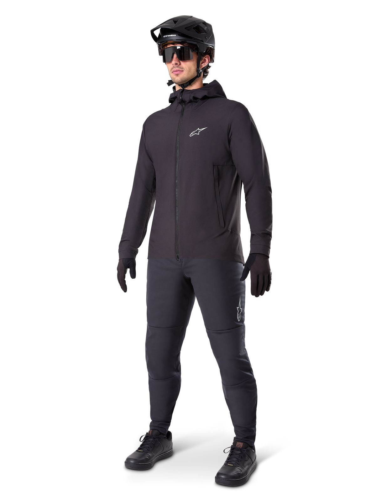 Alpinestars A-Dura Thermal Jacket in Black, worn by a male rider with complete mountain bike gear including a black helmet, sunglasses, and riding pants, lightweight insulated hooded jacket for cold-weather cycling performance.
