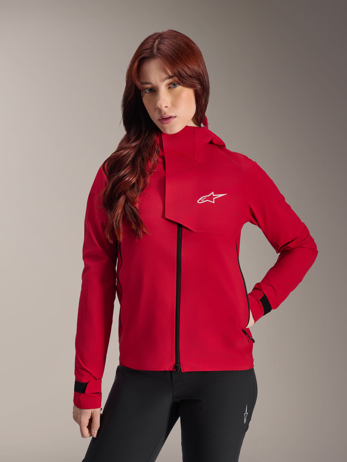 Alpinestars Stella A-Dura Elite Waterproof Jacket, damska kurtka rowerowa MTB, jaskrawoczerwona (Red Fluo), z przednią klapą przeciwdeszczową z białym logo Alpinestars, wysokim kołnierzem i regulowanymi mankietami, zestawiona z czarnymi spodniami dla technicznego kolarskiego wyglądu