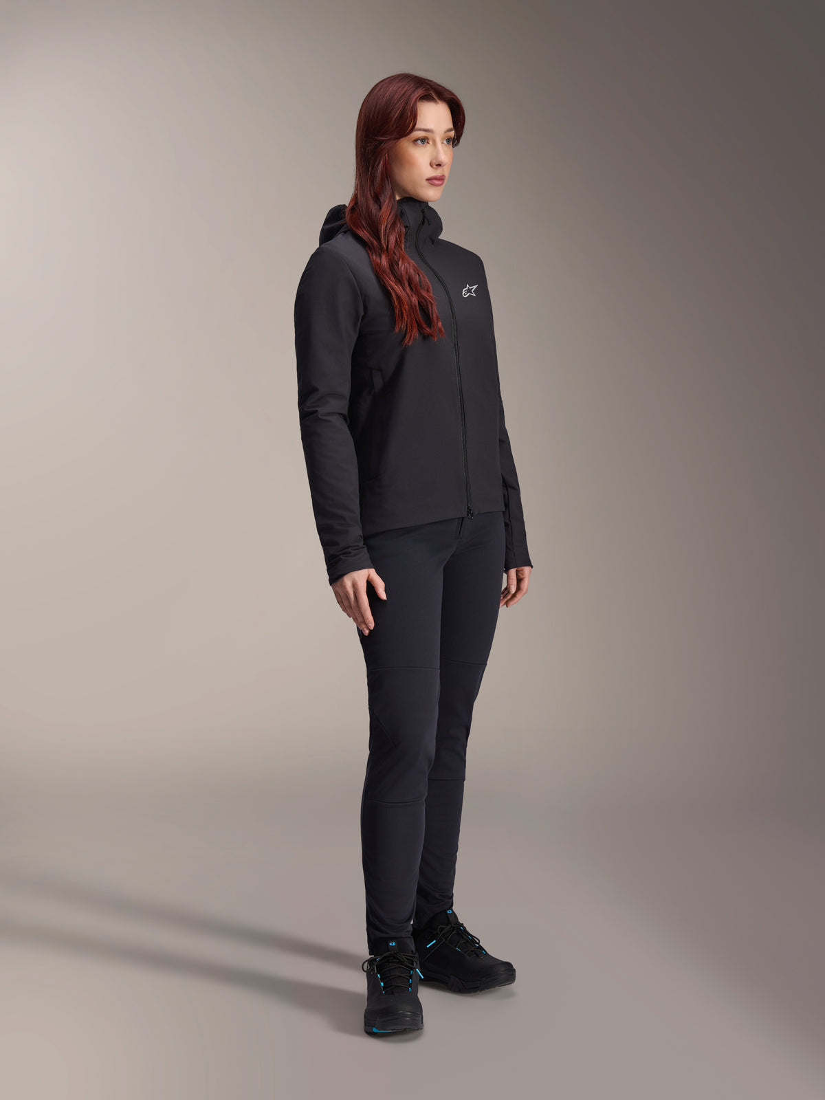 Alpinestars Stella A-Dura Thermal Jacket, damska czarna lekka kurtka ocieplana z kapturem, noszona z czarnymi spodniami i czarnymi butami, profesjonalny strój kolarski i MTB na zimne warunki