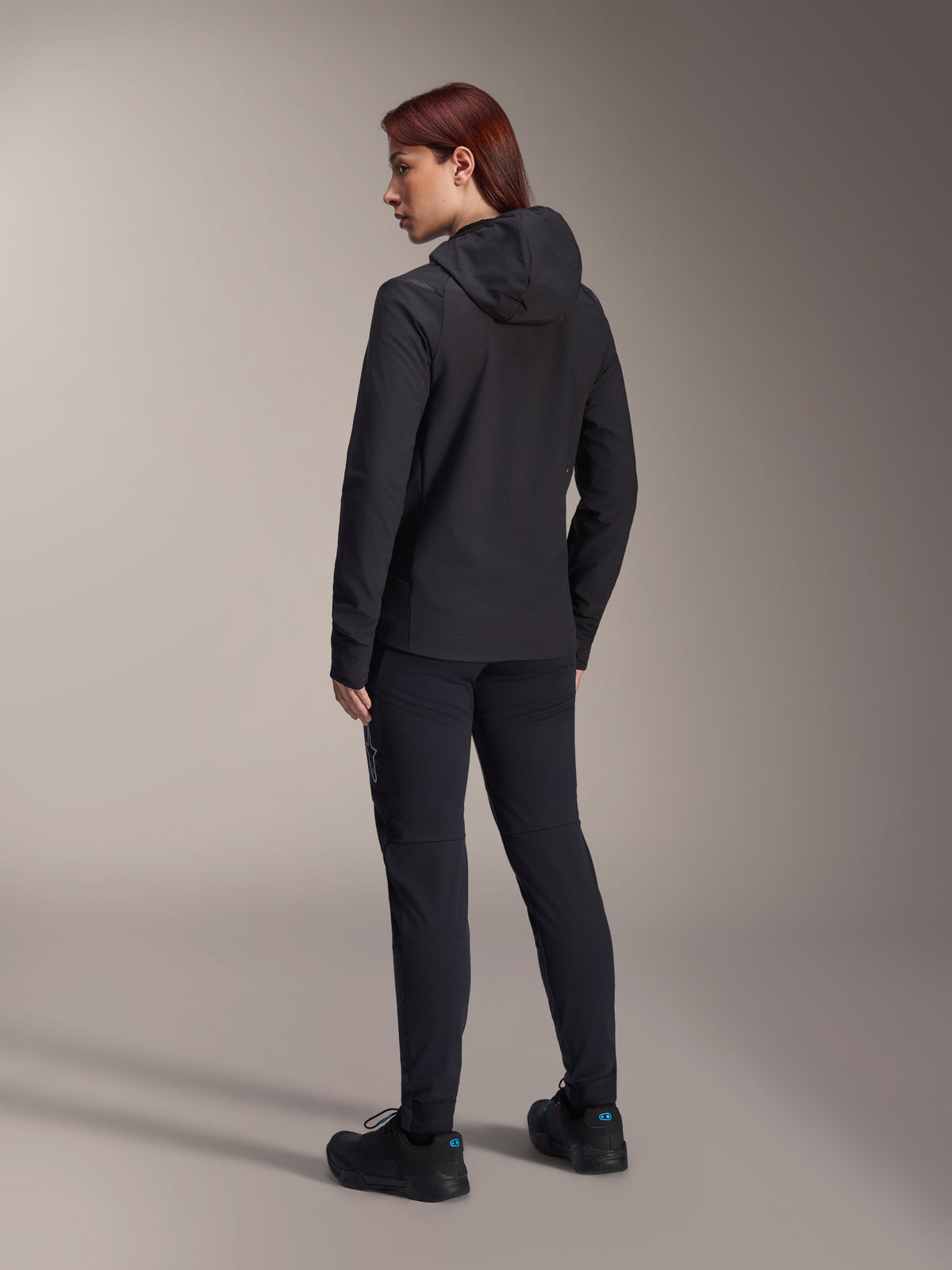 Alpinestars Stella A-Dura Thermal Jacket, damska kurtka rowerowa MTB, czarna, widok z tyłu podkreślający ocieplany kaptur i regularny krój, noszona z pasującymi czarnymi spodniami i butami, lekka izolacja termiczna do jazdy w zimne dni
