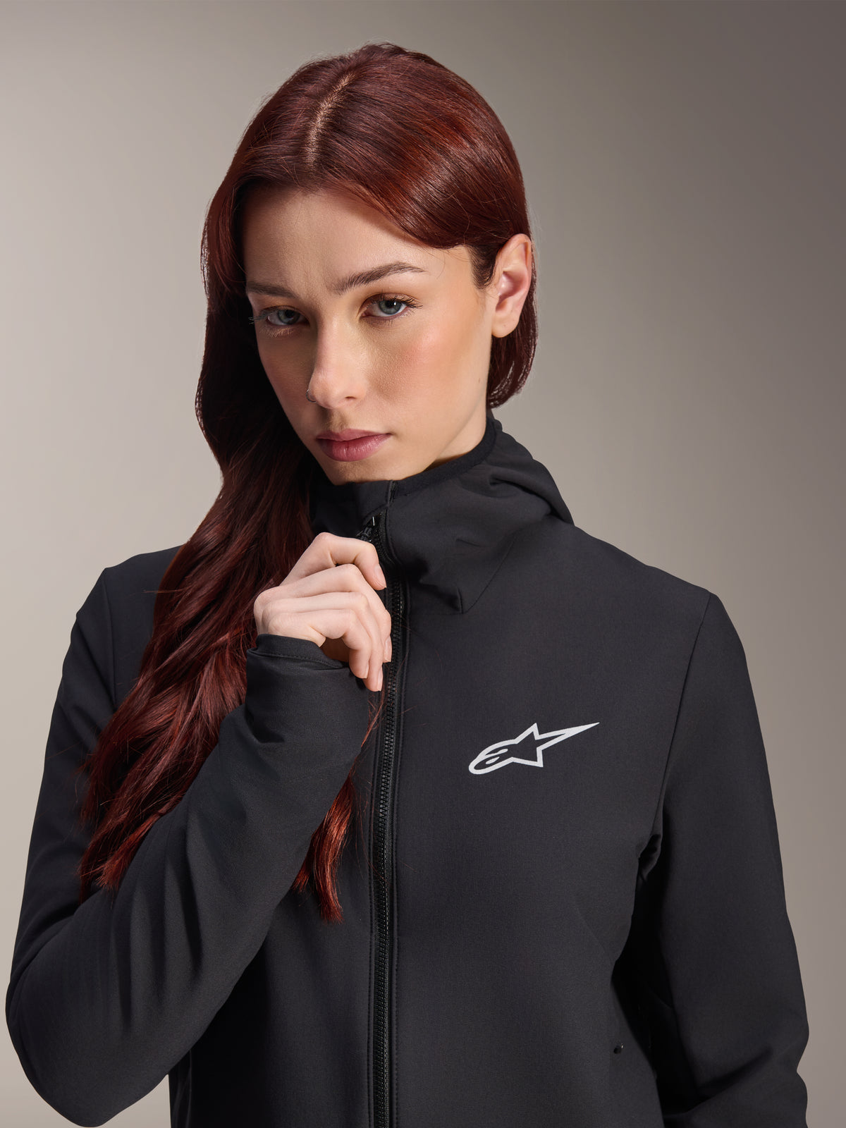 Alpinestars Stella A-Dura Thermal Jacket, damska czarna kurtka rowerowa, modelka z długimi rudobrązowymi włosami, białe logo Alpinestars na piersi, fason z kapturem i pełnym zamkiem błyskawicznym, odzież MTB