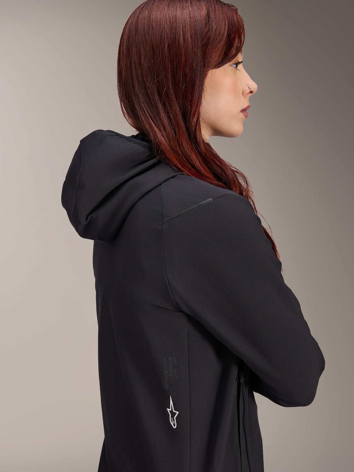 Kurtka Alpinestars Stella A-Dura Thermal, damska kurtka rowerowa, czarna, profil kobiety o rudych włosach ubranej w kurtkę, zintegrowany kaptur i białe logo gwiazdy Alpinestars z boku, lekka ocieplana odzież termiczna do MTB
