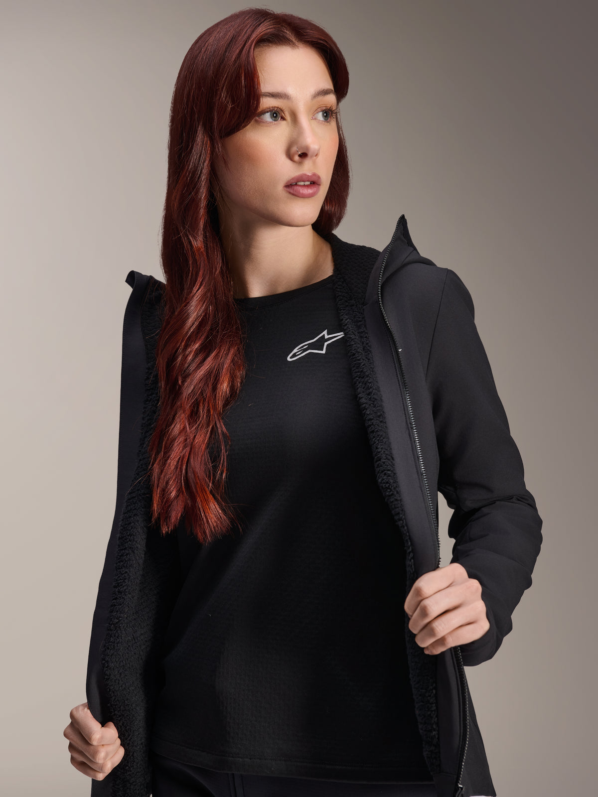 Alpinestars Stella A-Dura Thermal Jacket, damska czarna kurtka rowerowa, pokazana jako rozpięta z teksturowaną podszewką polarową i przodem zapinanym na zamek, założona na czarny t-shirt z logo Alpinestars, lekka i ocieplona, idealna do jazdy w niskich temperaturach