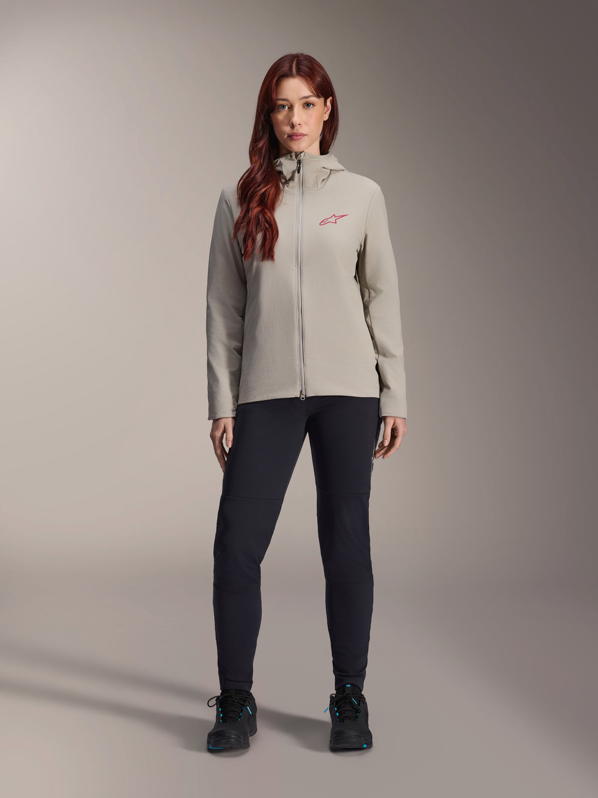 Damska kurtka Alpinestars Stella A-Dura Thermal, kurtka MTB, szary Titanium, noszona z czarnymi spodniami technicznymi i czarnym obuwiem, z kapturem wyściełanym polarem i czerwonym logo na piersi, przeznaczona do jazdy w niskich temperaturach