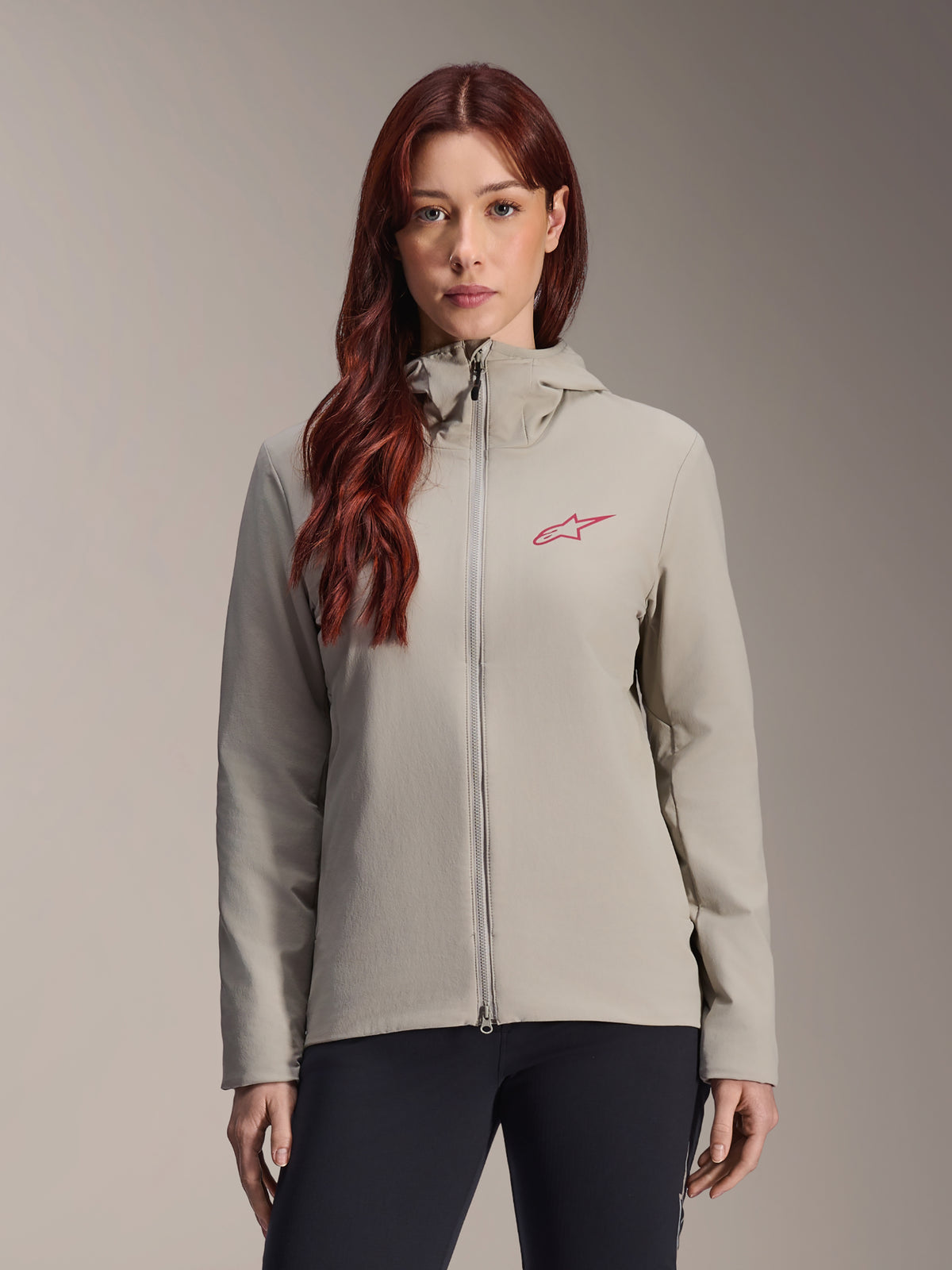 Alpinestars Stella A-Dura Thermal Jacket, damska kurtka termiczna, szary Titanium, model z kapturem i zamkiem błyskawicznym, czerwone logo gwiazdy na piersi, w zestawieniu z czarnymi spodniami, lifestylowy portret studyjny