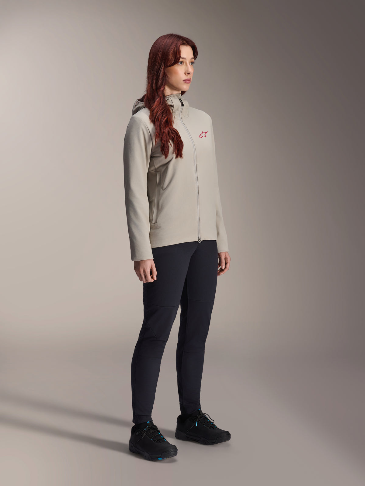 Alpinestars Stella A-Dura Thermal Jacket, szara damska kurtka rowerowa ocieplana, czerwone logo z gwiazdą na klatce piersiowej, czarne spodnie techniczne i czarne buty MTB, zdjęcie studyjne odzieży rowerowej