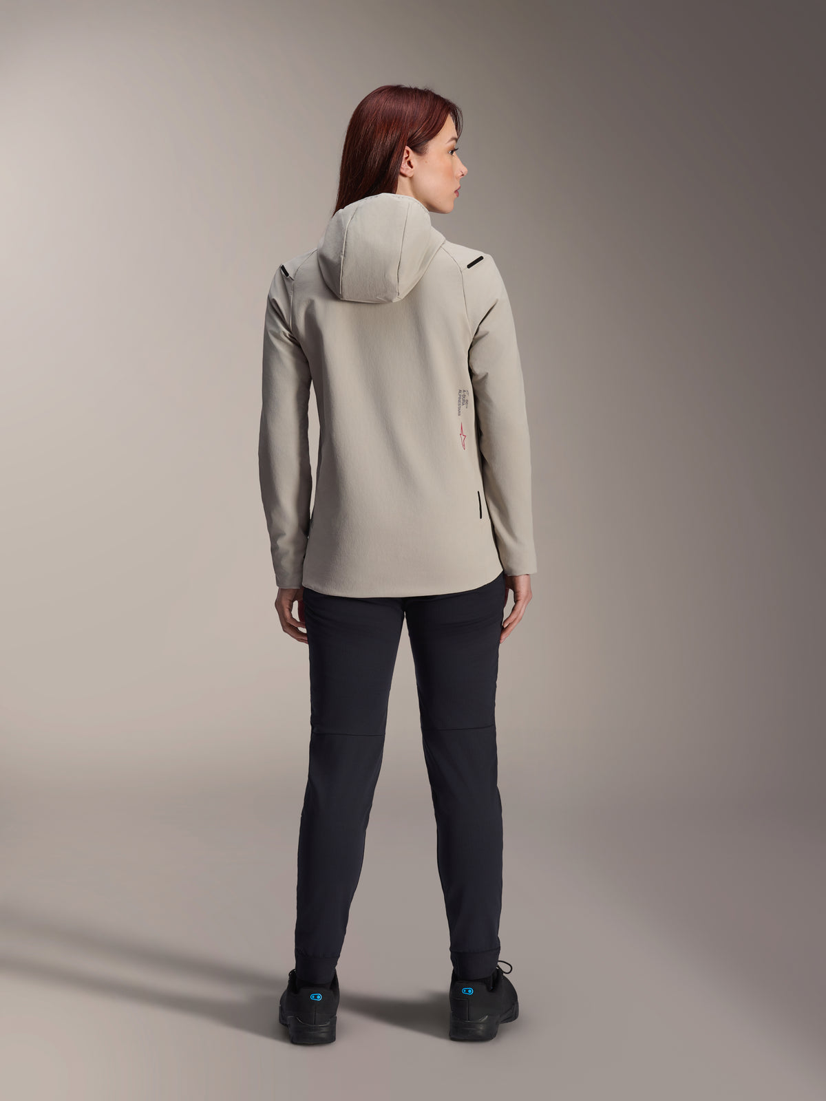 Alpinestars Stella A-Dura Thermal Jacket, damska kurtka w kolorze szarym (Titanium Gray), widok z tyłu z czarnymi spodniami, ocieplany kaptur z polarową wyściółką i małe czerwone logo, funkcjonalna i stylowa kurtka MTB na zimne dni