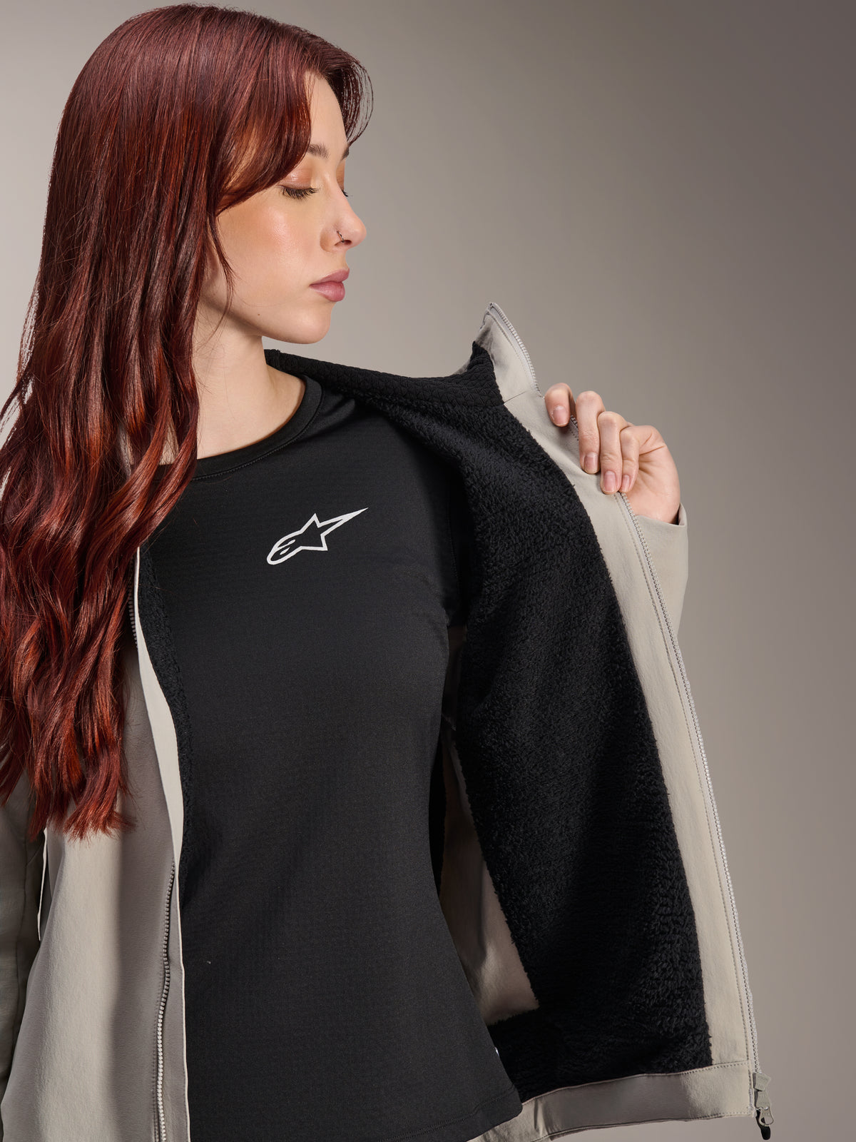 Kobieta w kurtce Alpinestars Stella A-Dura Thermal w kolorze Titanium, prezentująca czarną teksturowaną podszewkę z polaru, założona na czarny t-shirt z białym logo gwiazdy, lekka kurtka MTB na zimne dni.