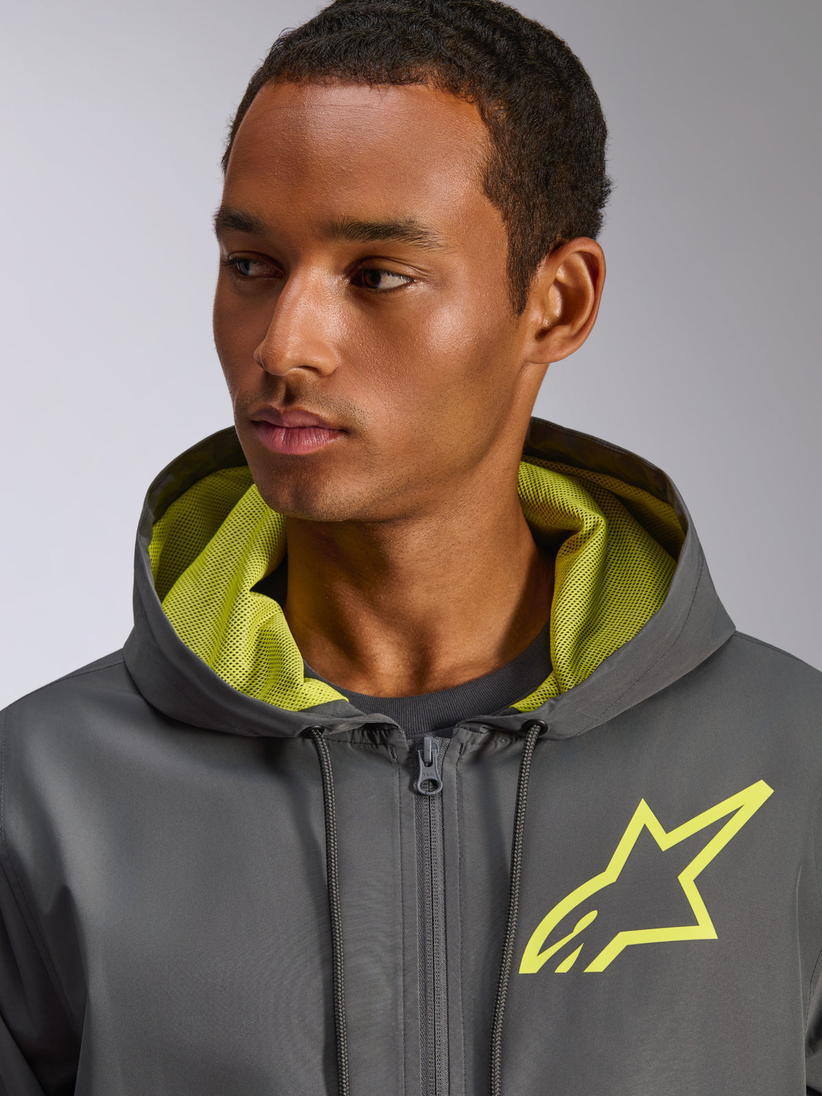 Alpinestars Speeder Chromium Windbreak Jacket, ciemnoszara z neonowożółtymi akcentami, żółte logo z gwiazdą na piersi i dopasowana podszewka kaptura z siateczki, lekka wiatrówka casualowa