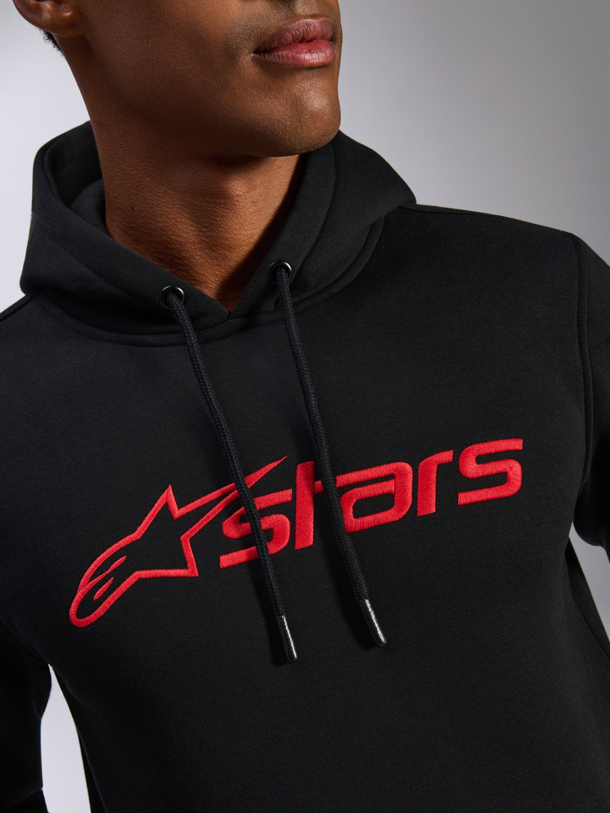 Alpinestars Blaze V3 Hoodie, zbliżenie na klatkę piersiową, czarna tkanina polarowa z czerwonym linearnym nadrukiem logo, kaptur ze sznurkami z powlekanymi końcówkami, codzienna odzież streetwearowa inspirowana motorsportem