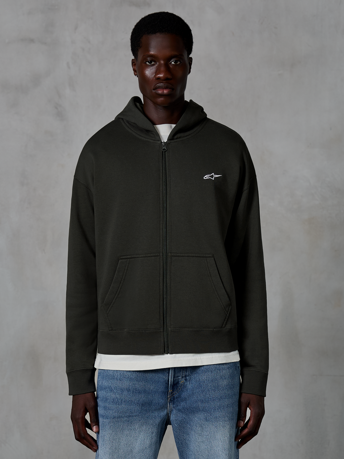 Alpinestars Essentials Ageless Zip Hoodie, rozpinana bluza z kapturem, kolor Off Black, małe białe logo gwiazdy na piersi, przednie kieszenie, ściągacze przy mankietach, codzienna odzież uliczna inspirowana sportami motorowymi