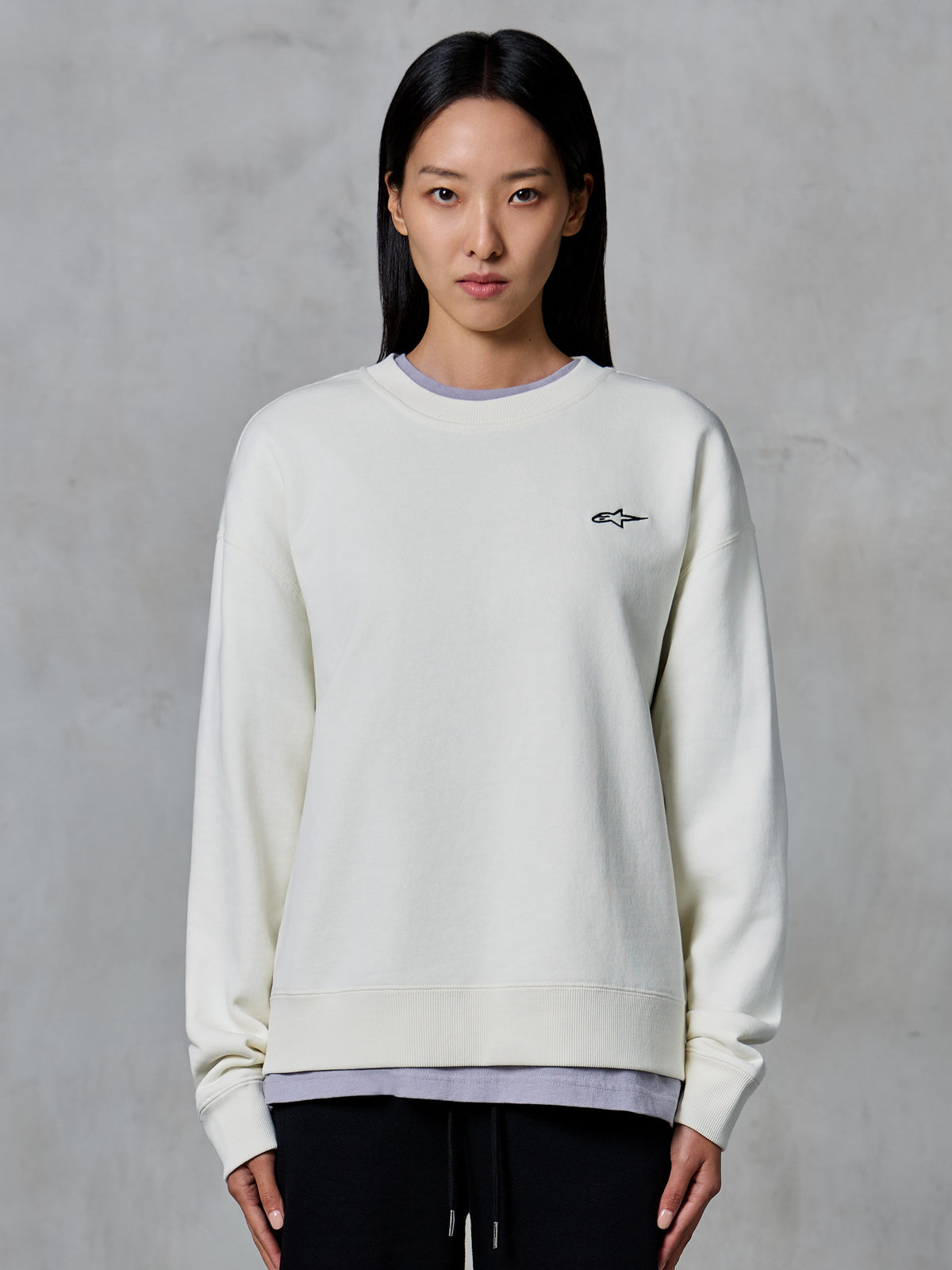 Alpinestars Essentials Ageless Crew, bluza z okrągłym dekoltem, kolor złamanej bieli, małe czarne logo Alpinestars na piersi, casualowa odzież lifestyle prezentowana na kobiecie