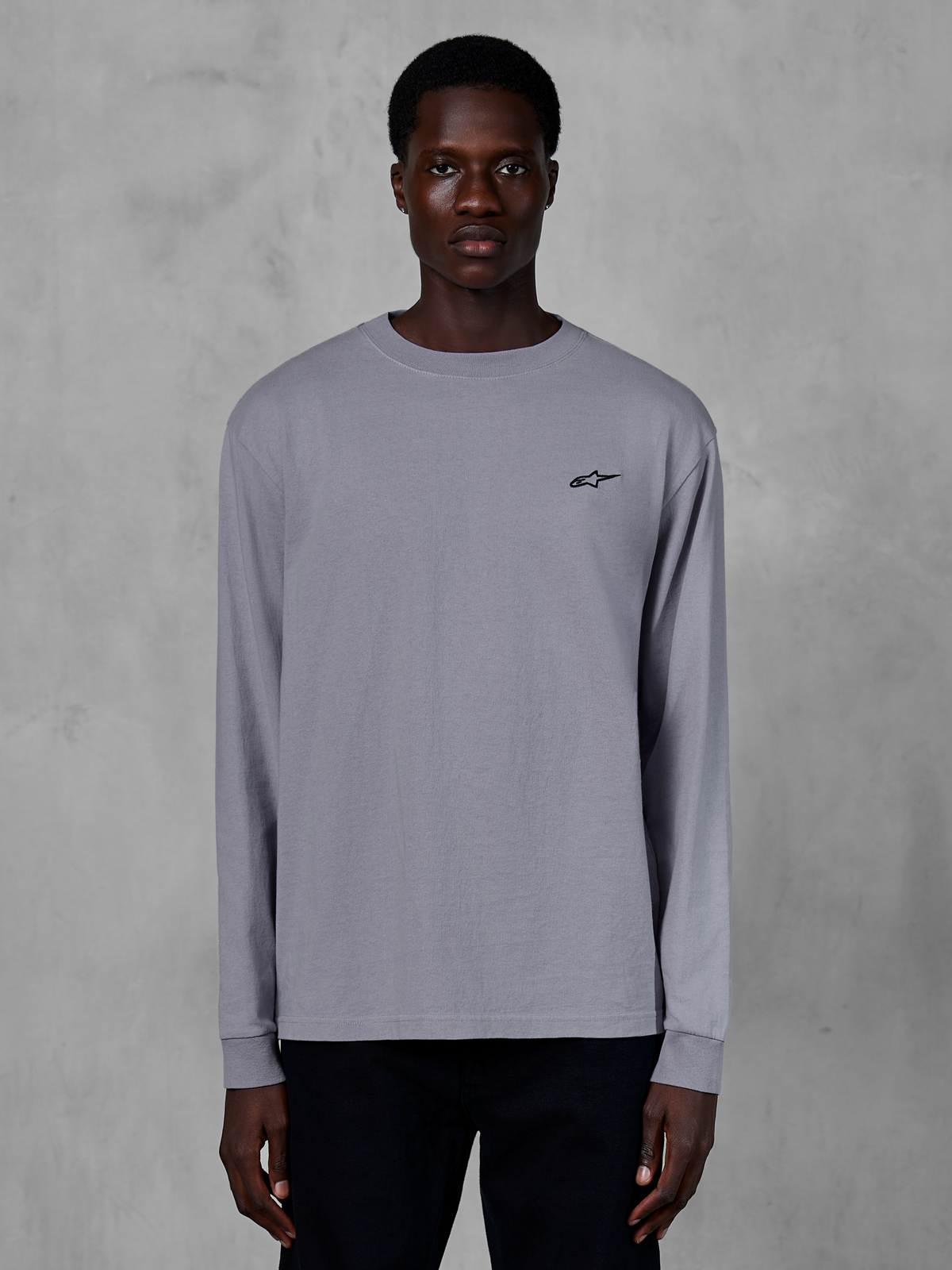Alpinestars Essentials Ageless LS Tee, srebrna koszulka z długim rękawem, prezentowana na modelu, z małym czarnym logo Alpinestars na piersi, luźny nowoczesny krój, codzienna odzież streetwearowa z bawełny organicznej