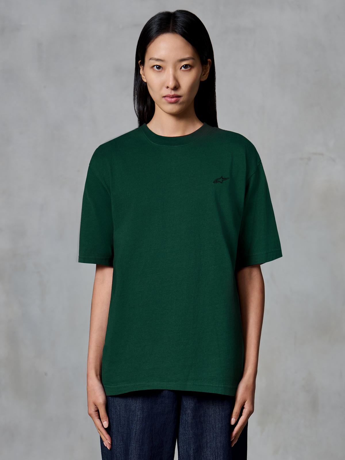 Alpinestars Essentials Ageless SS Tee, koszulka z krótkim rękawem, kolor Pine Green, prezentowana na modelce, małe czarne logo na piersi, luźny krój, bawełna organiczna, casualowy streetwear