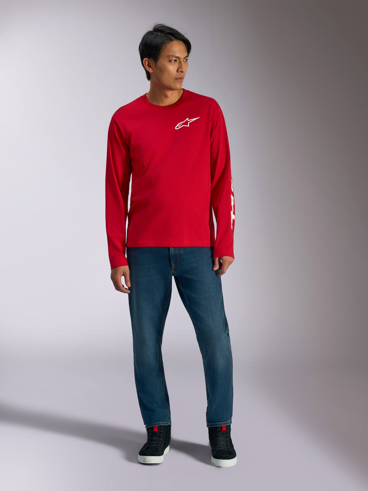 Alpinestars Trackside CSF Tee, koszulka z długim rękawem, czerwona z białym logo Alpinestars, ujęcie lifestyle w niebieskich jeansach i czarnych sneakersach, codzienna odzież sportowa inspirowana motorsportem