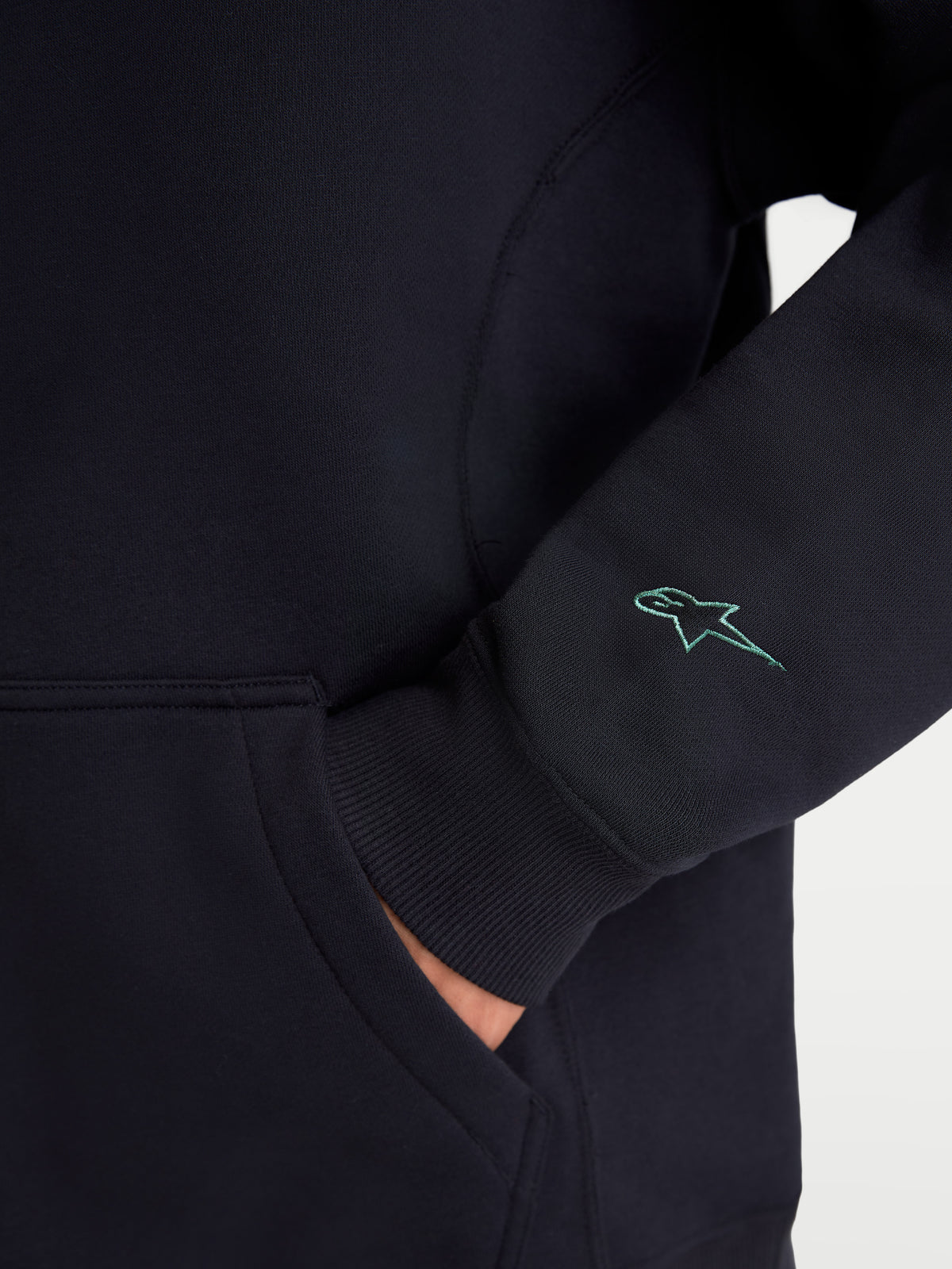 Alpinestars Bluza Guise Oversize, czarna bluza sportowa z polaru, zbliżenie na haftowane logo Astars na rękawie, prążkowany mankiet i detal kieszeni kangurki, mieszanka bawełny i poliestru z recyklingu, swobodny krój oversize.
