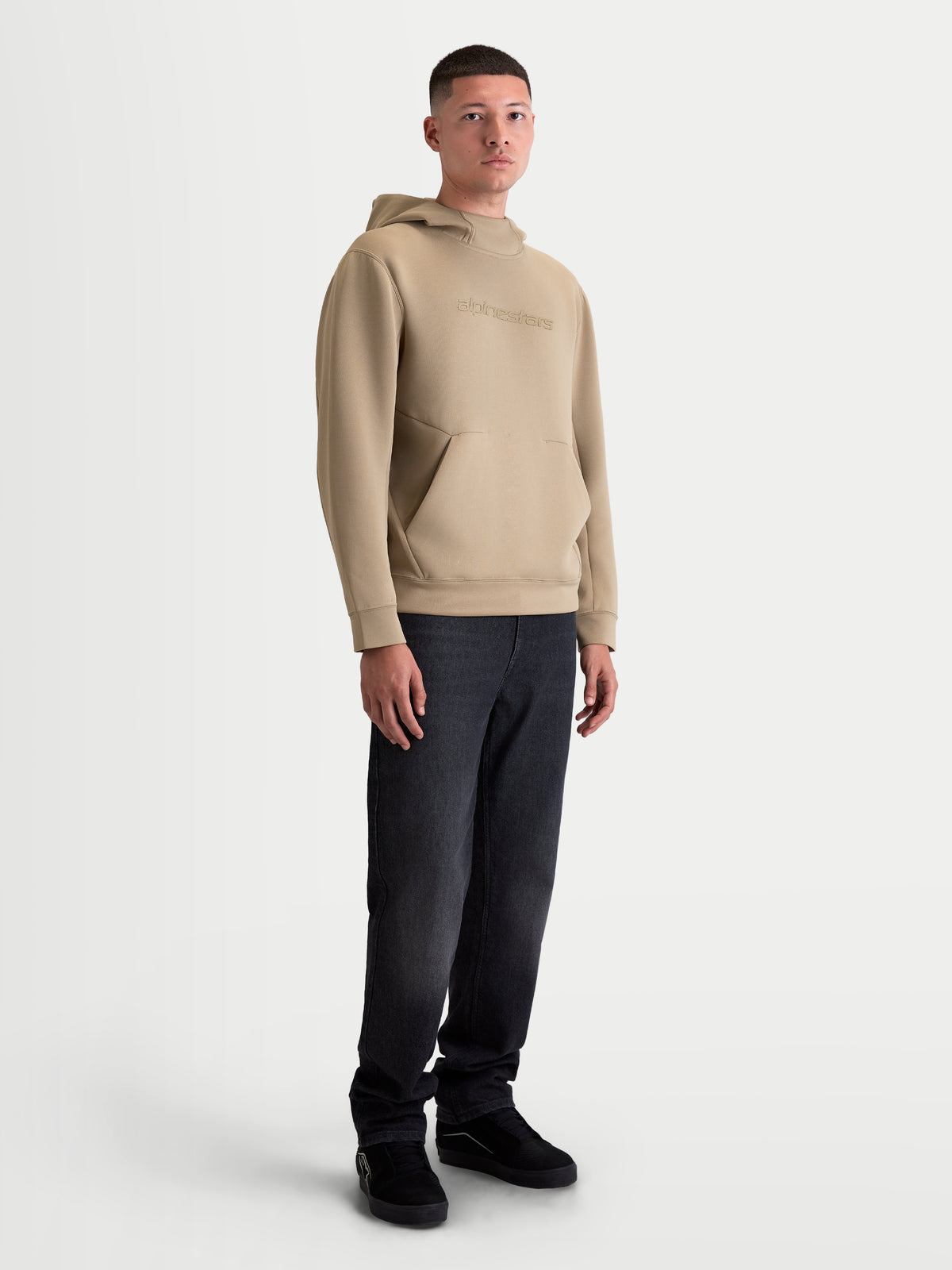 Alpinestars bluza z kapturem Datrix, męska bluza sportowa typu pullover, beżowa, tonalne logo HD, przednia kieszeń z zaszewkami i kaptur z siatkową podszewką, styl casual inspirowany motorsportem, pokazana na modelu.