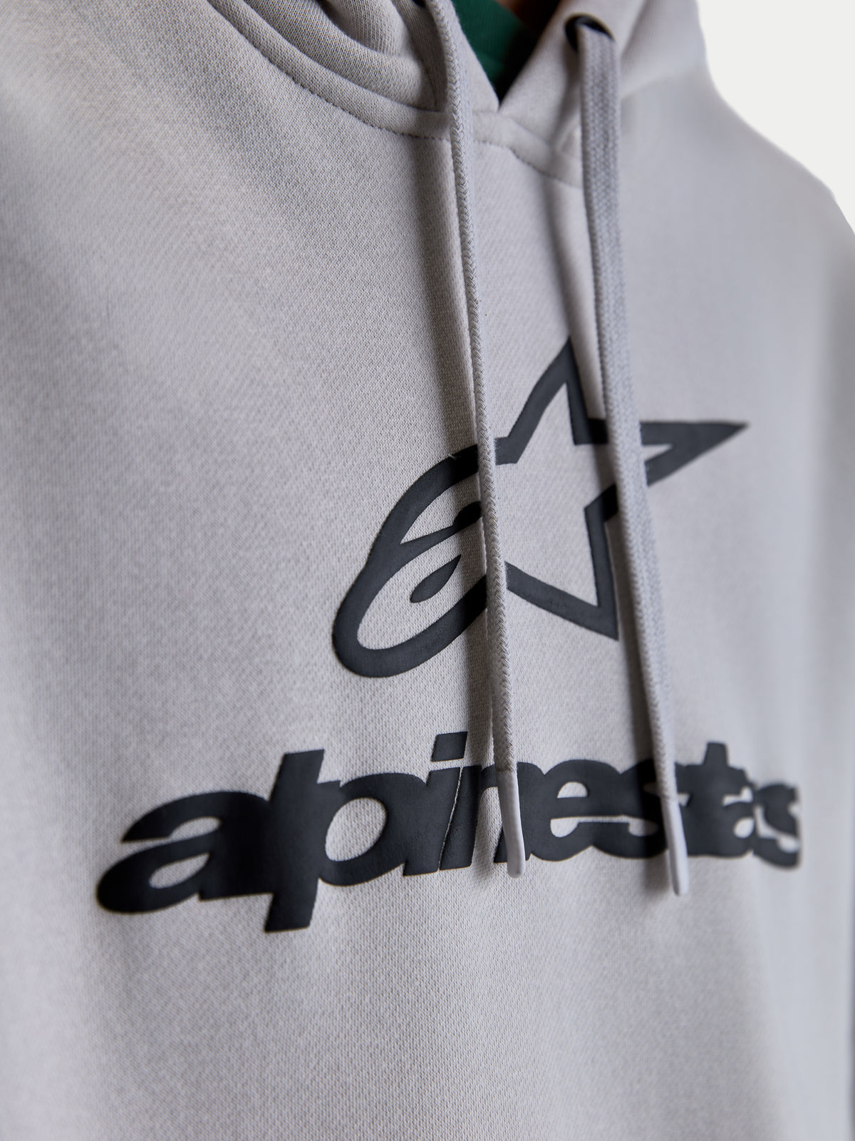 Alpinestars bluza z kapturem Prelude Oversize, zbliżenie na czarny wypukły nadruk logo puff print na szarym polarze, płaskie sznurki, premium odzież sportowa lifestyle.