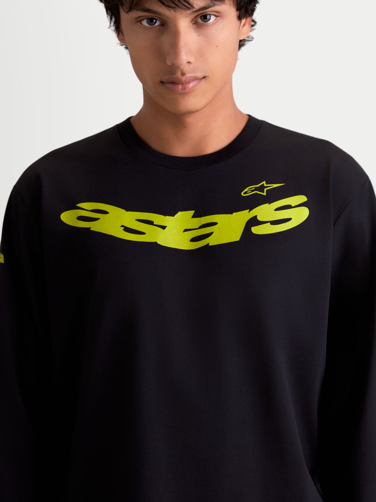 Alpinestars koszulka Velocifier CSF, czarna męska koszulka z długim rękawem na modelu, żółta zakrzywiona grafika Astars na piersi i logo na ramieniu, casualowa odzież sportowa, mieszanka bawełny