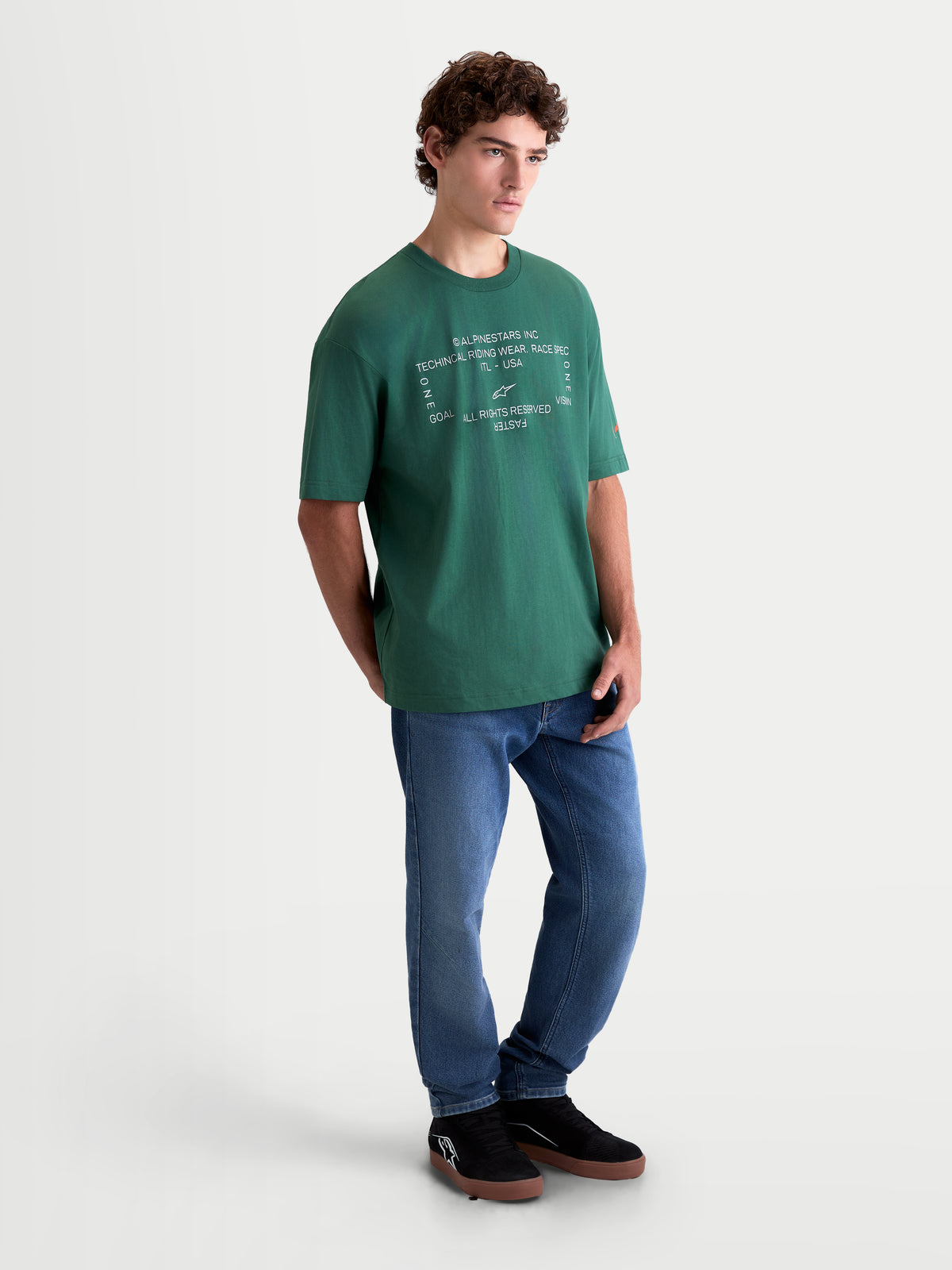 Alpinestars Koszulka Infinity Oversized CSF, męska koszulka z krótkim rękawem, zielona, krój oversize, biała techniczna grafika z przodu, casualowa odzież sportowa w stylu motorsport, model w niebieskich jeansach