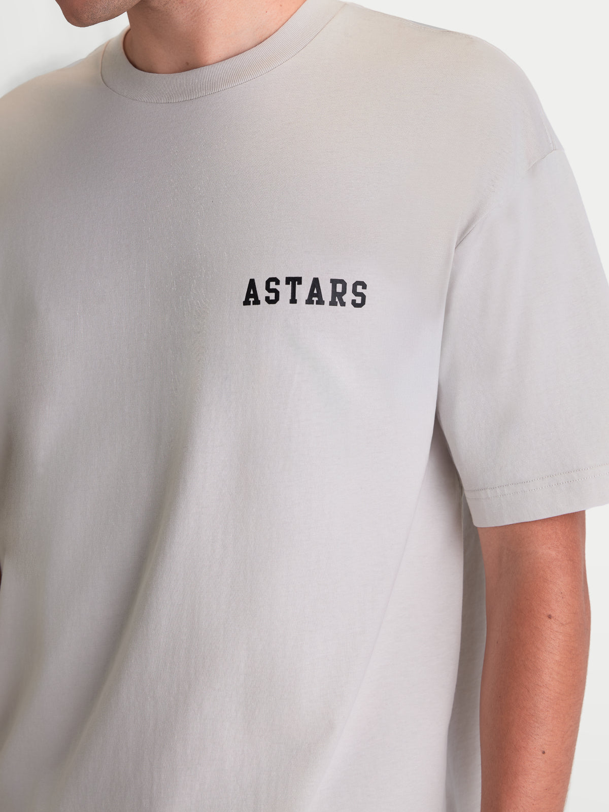 Alpinestars koszulka Latitude Oversized CSF, szara koszulka z krótkim rękawem, czarny napis ASTARS na piersi, swobodny krój oversized, miękka mieszanka bawełny i poliestru, casualowa odzież sportowa, widoczna na modelu.