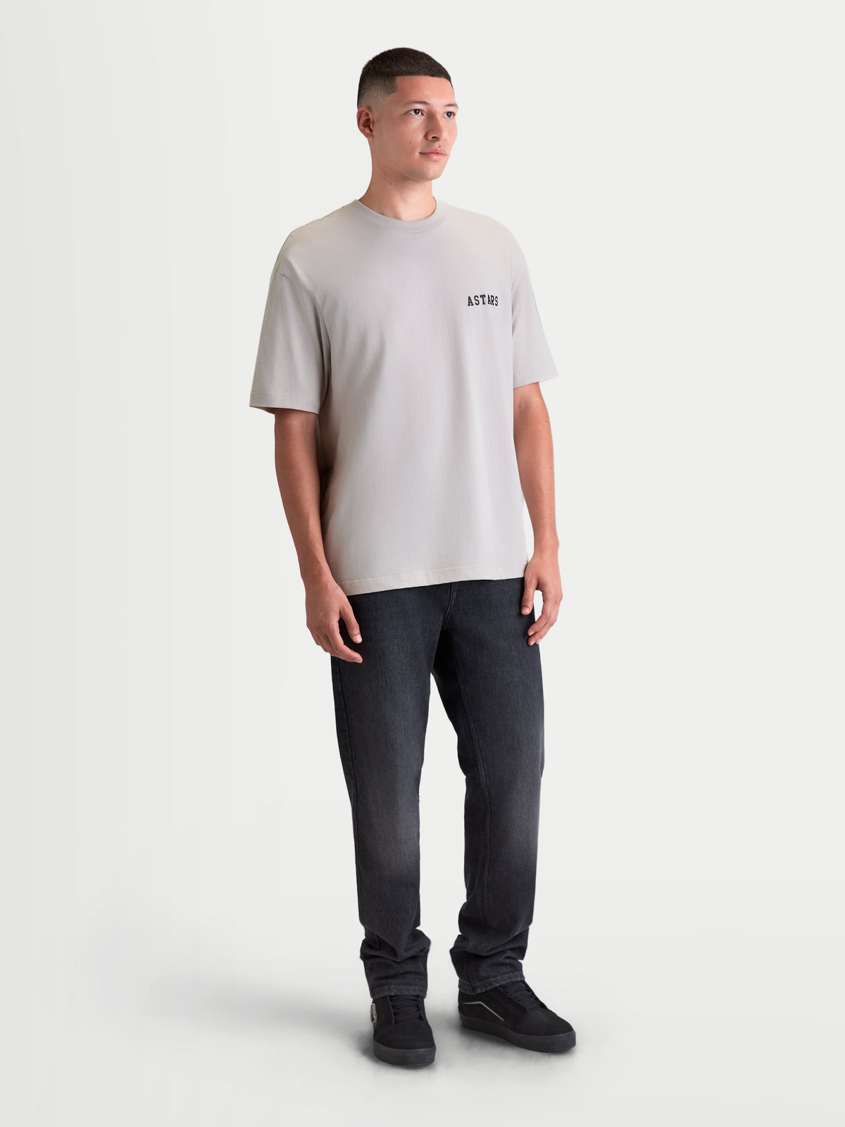 Alpinestars koszulka Latitude Oversized CSF, szara koszulka z krótkim rękawem na modelu, swobodny krój oversized z czarnym logotypem ASTARS na piersi, casualowa odzież sportowa z mieszanki bawełny i poliestru.