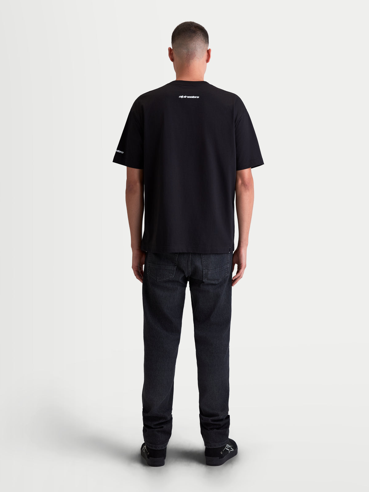 Alpinestars Mandate Oversized CSF, czarna koszulka z krótkim rękawem, odzież sportowa, widok z tyłu na modelu, białe grafiki puff print na karku i rękawie, luźny krój oversize, mieszanka bawełny i poliestru.
