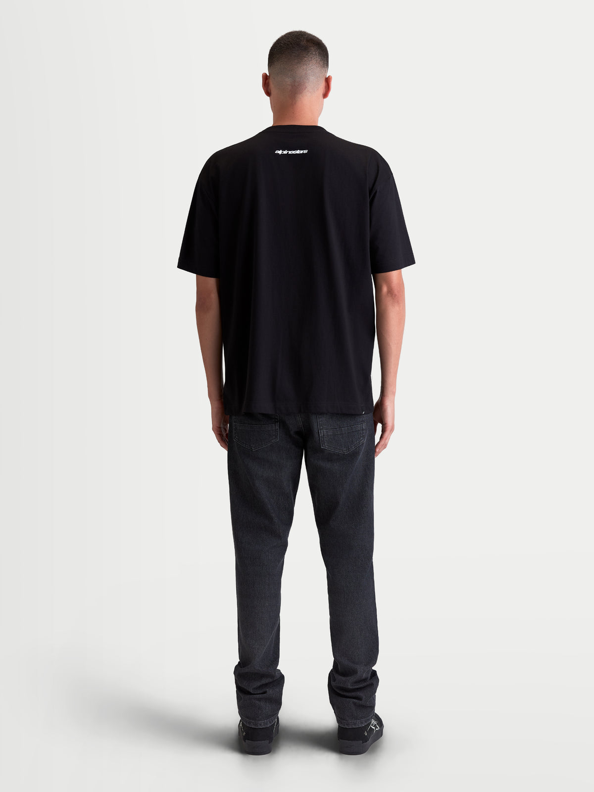 Alpinestars Prelude Oversized CSF Tee, czarna koszulka z krótkim rękawem, widok z tyłu na modelu, białe logo z napisem Alpinestars na górze pleców, miękka mieszanka bawełny i poliestru, odzież sportowa.
