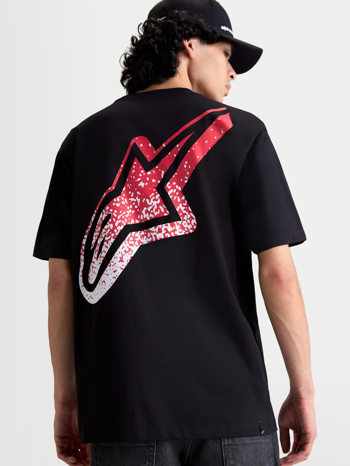 Alpinestars Koszulka Meteor CSF, czarna koszulka z krótkim rękawem, widok z tyłu na modelu, duża czerwono-biała grafika logo Astars z gradientem w stylu MX, casualowa odzież sportowa.