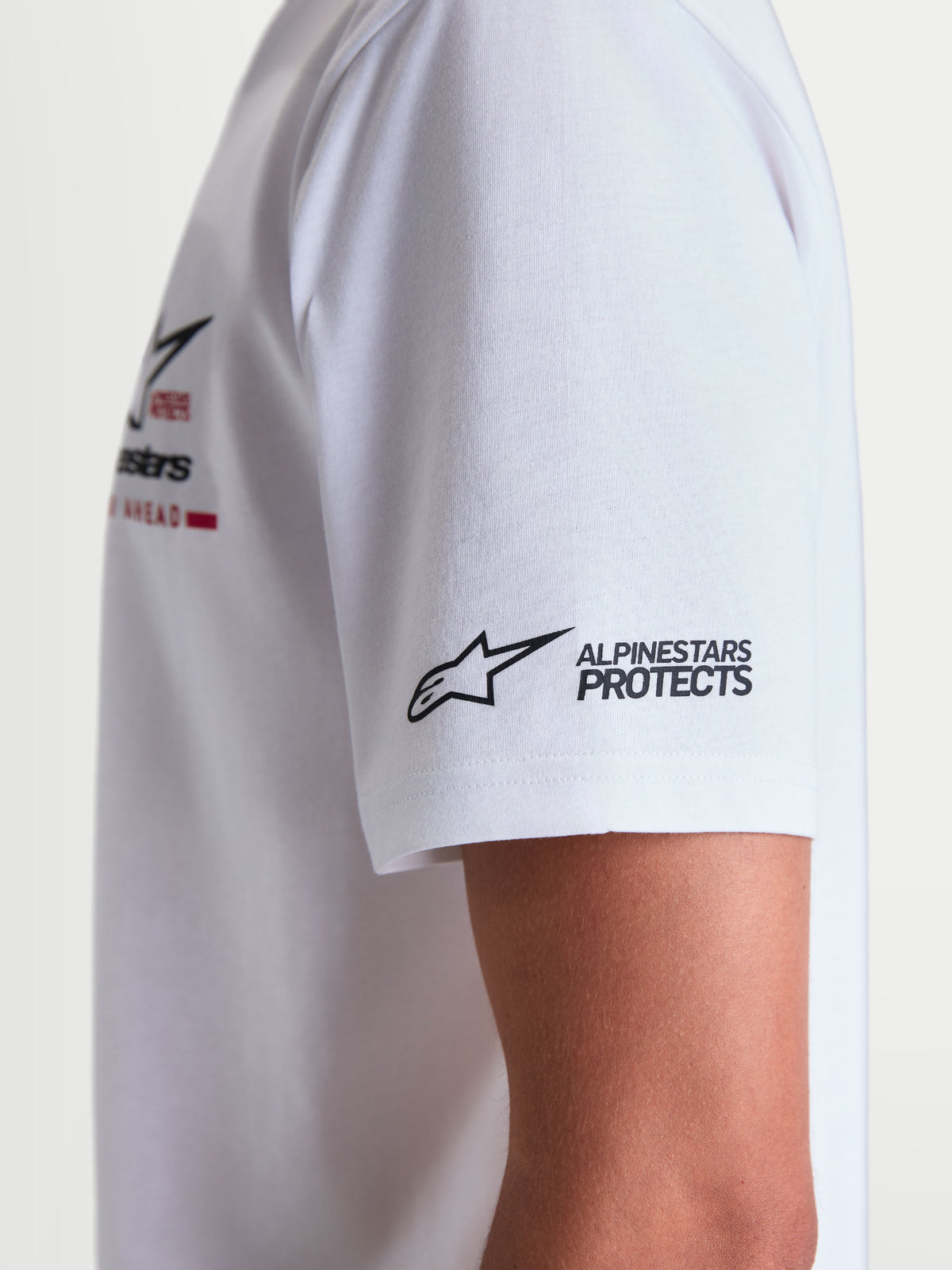 Alpinestars Koszulka P1 CSF, biała koszulka z krótkim rękawem, zbliżenie na detale nadruku logo Alpinestars PROTECTS na rękawie, mieszanka bawełny i poliestru 60/40, casualowa odzież sportowa dla mężczyzn i kobiet.