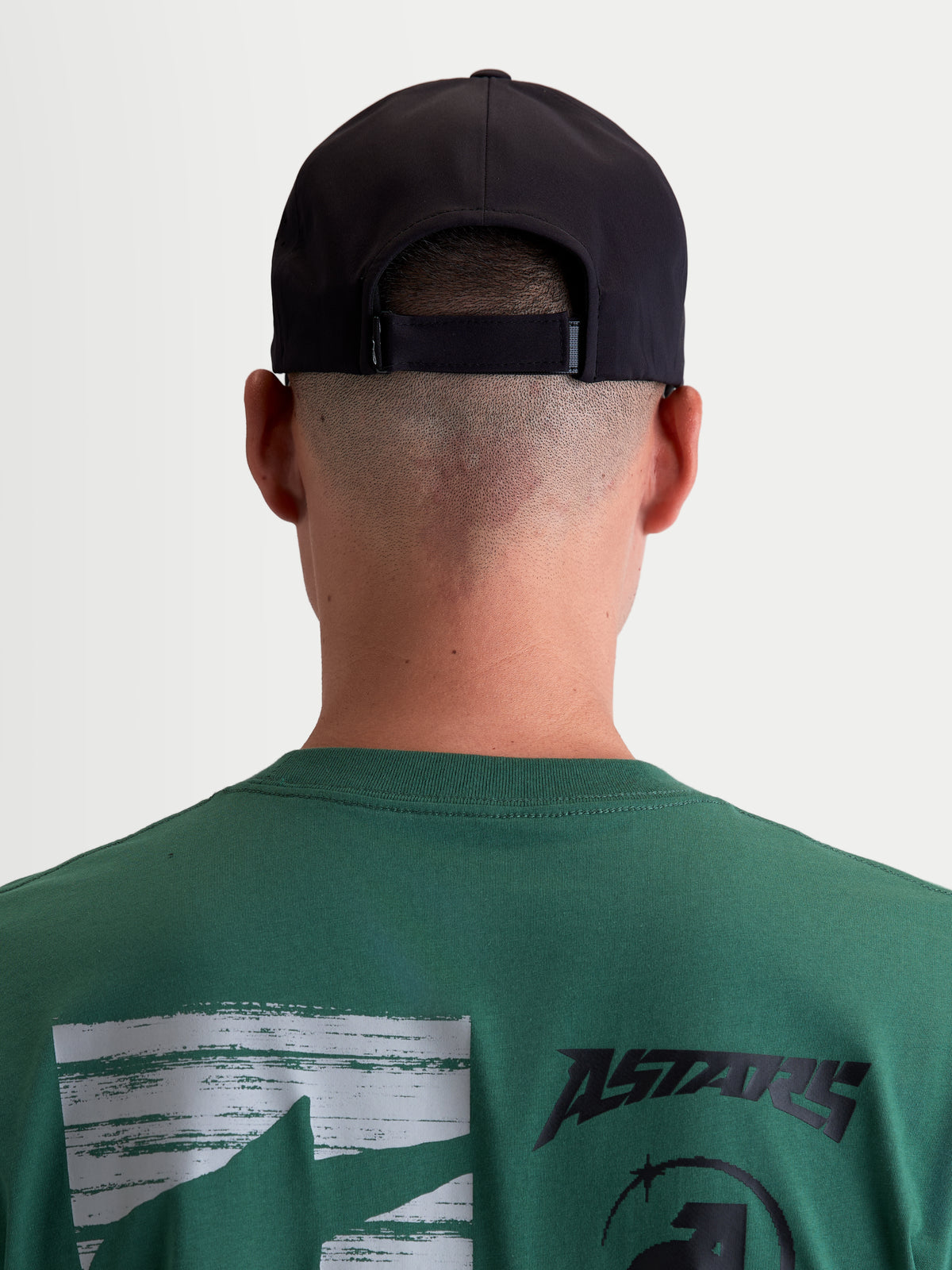 Alpinestars czapka Algo Perf Adjustable, czarna czapka z daszkiem inspirowana motorsportem, widok z tyłu na modelu pokazujący regulowane zapięcie, techniczna konstrukcja materiału, odzież sportowa unisex.