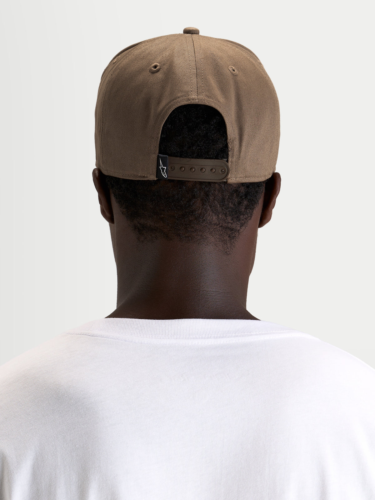 Alpinestars Czapka Acme Snapback, brązowa czapka z daszkiem sportswear na modelu, widok z tyłu pokazujący regulowane zapięcie snapback i tylną etykietę z logo