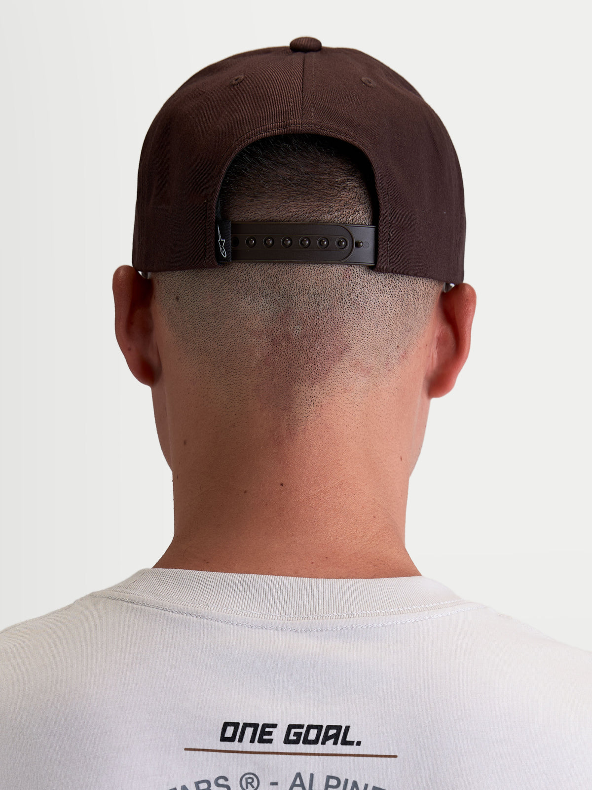 Alpinestars Czapka Combo Logo Snapback, brązowa czapka z daszkiem typu snapback, casualowa odzież sportowa motorsport, widok z tyłu na modelu, regulowane zapięcie snapback i markowa metka, konstrukcja z trwałego kepru.