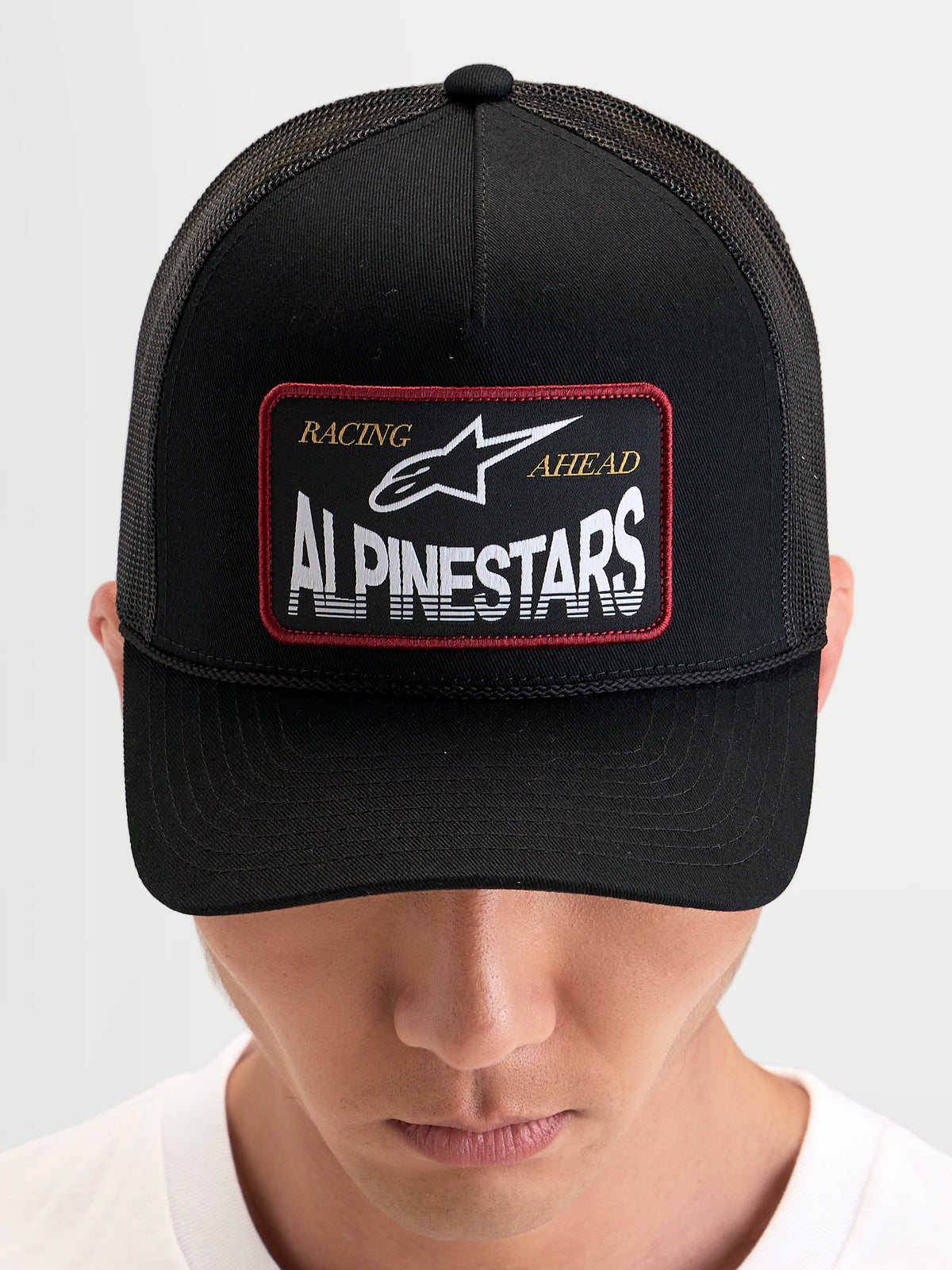 Alpinestars Hemmings Trucker, czapka z daszkiem sportswear, czarna, z przodu tkana naszywka z logo Alpinestars i z tyłu oddychające panele z siatki, na modelu
