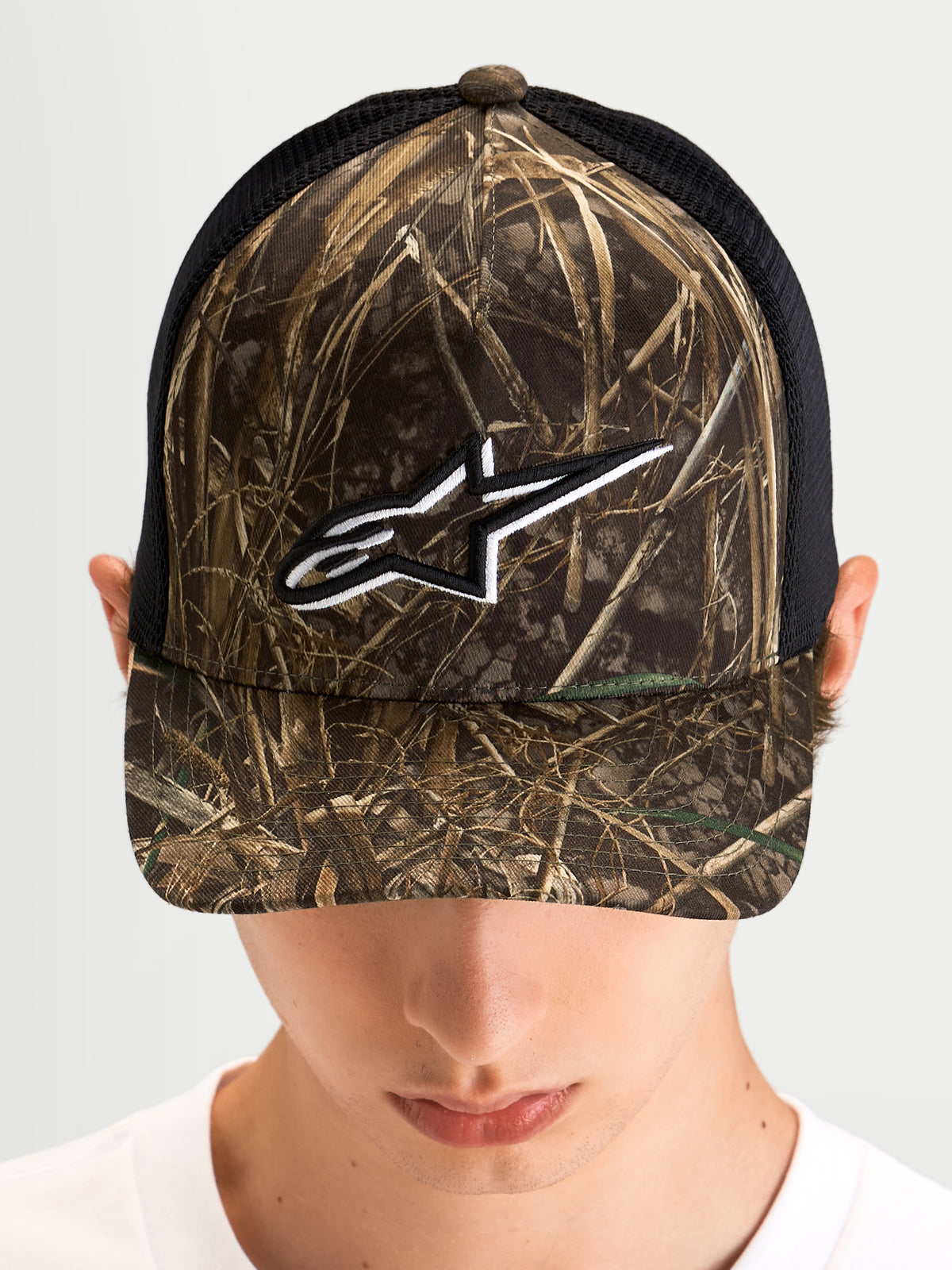 Alpinestars Czapka Z Daszkiem Thicket Realtree, czapka z daszkiem typu trucker w kamuflażu Realtree i czarnym kolorze, na modelu, z usztywnioną koroną i białym haftowanym logo Astars na froncie