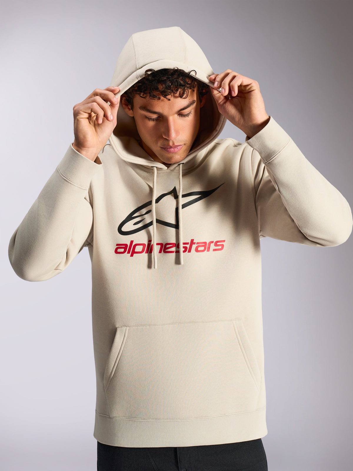 Alpinestars Always V3 Hoodie, męski model w kremowej bluzie polarowej, czarno-czerwone liniowe logo z przodu, kaptur ze sznurkiem, kieszeń typu kangurka, codzienna odzież uliczna inspirowana sportami motorowymi
