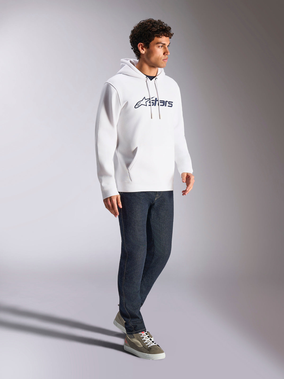 Alpinestars Blaze V3 Hoodie, White and Navy, casual streetwear worn by a model with dark blue jeans and sneakers, features a drawstring hood and bold front logo print, modern motorsport-inspired design