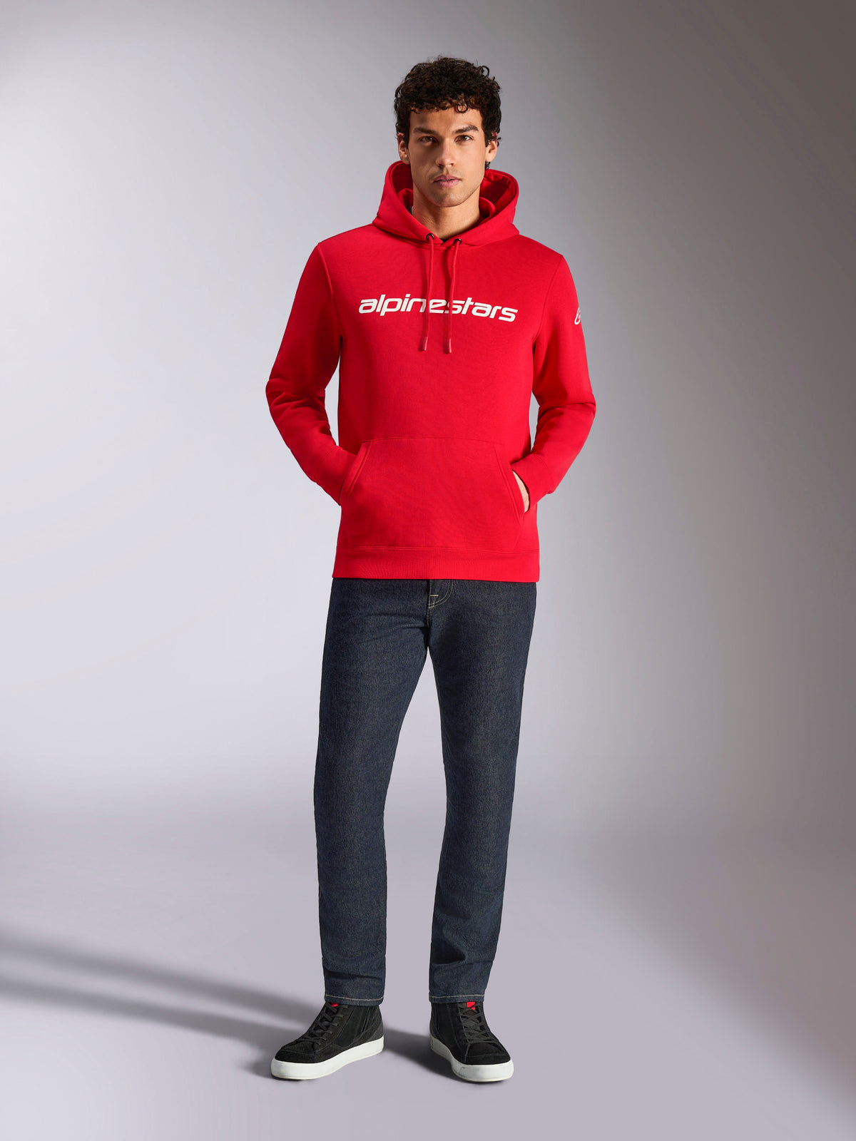 Alpinestars Linear Wordmark V3 Hoodie, casual streetwear, red with white linear wordmark on the chest, drawstring hood, front pouch pocket, worn with dark jeans and black sneakers, modern motorsport-inspired design