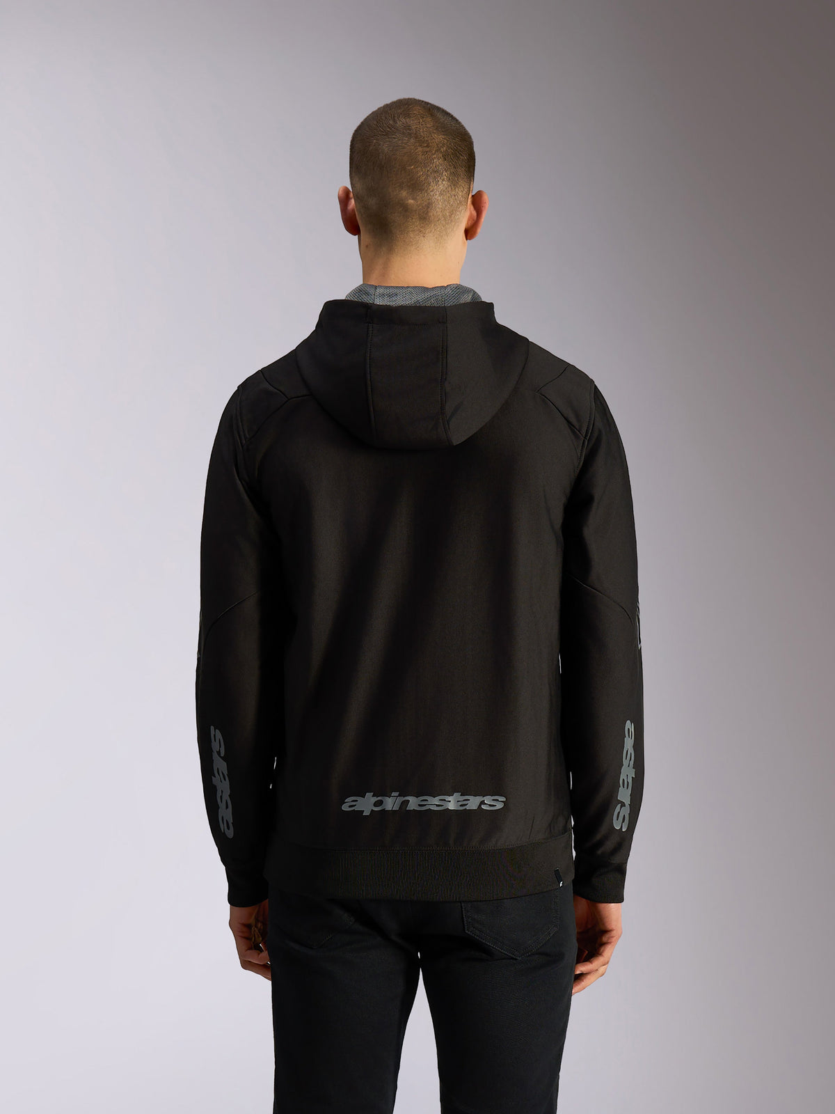 Alpinestars Sessions V3 Hoodie, widok od tyłu, czarna rozpinana bluza z kapturem, szary napis Alpinestars na dole pleców, logo Astars na rękawach, ściągacze na dole i przy mankietach, codzienna odzież streetwearowa w stylu motorsportowym