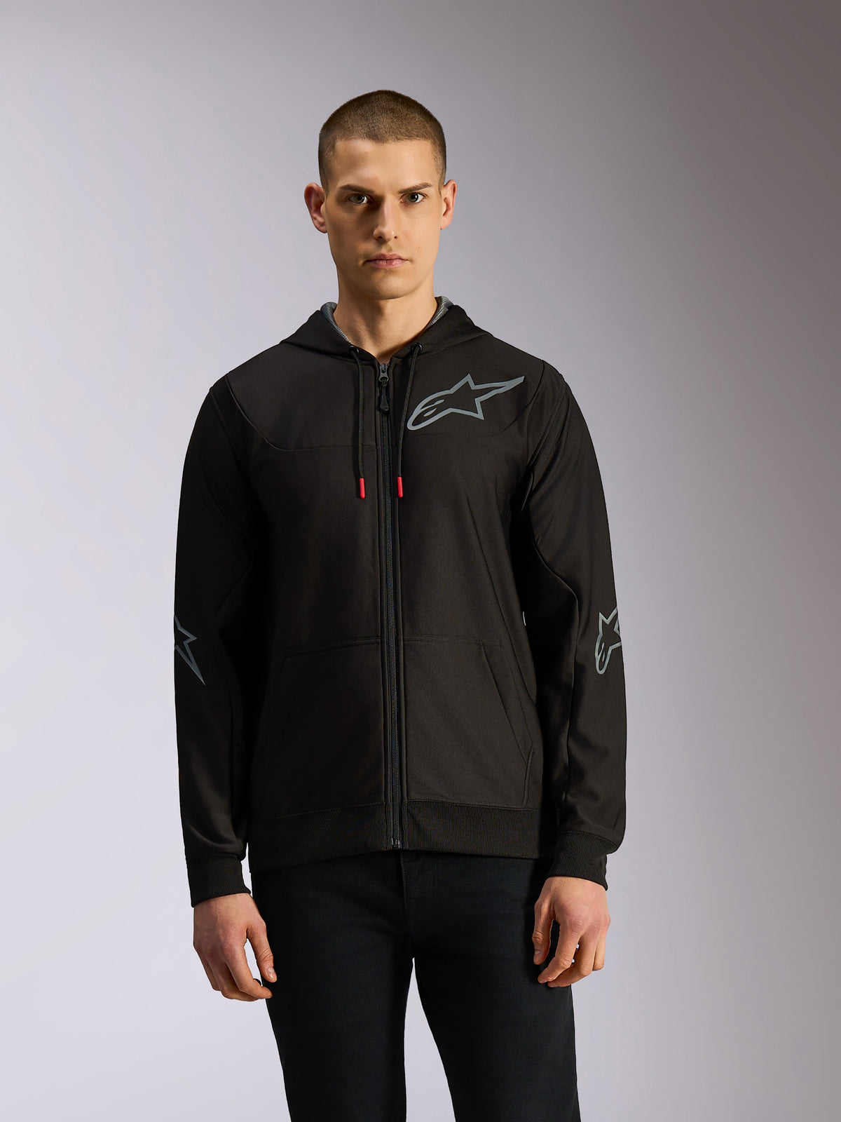 Alpinestars Sessions V3 Hoodie, bluza z polaru zapinana na zamek w kolorze czarnym i szarym, z szarymi logotypami gwiazdy na piersi i łokciach, techniczne sznurki z czerwonymi końcówkami, codzienny styl streetwearowy inspirowany motorsportem
