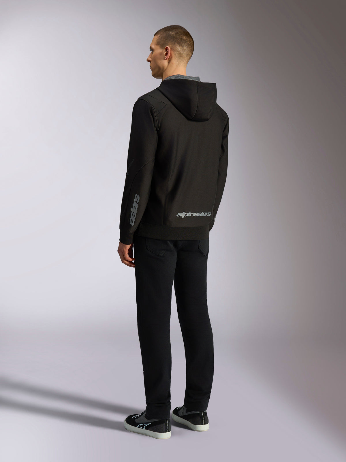 Alpinestars Sessions V3 Hoodie, codzienna odzież streetwearowa w stylu motorsport, czarna z szarym napisem na dole pleców i przedramieniu, rozpinana bluza z polaru z kapturem z podszewką z siatki, widok z tyłu na modelu, nowoczesny sportowy design