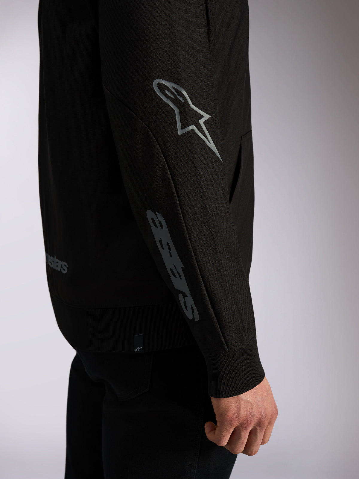 Bluza z kapturem Alpinestars Sessions V3, czarna odzież streetwearowa, zbliżenie na rękaw z szarym logo Astars na łokciu i logotypem na przedramieniu, prążkowane ściągacze, design inspirowany sportami motorowymi