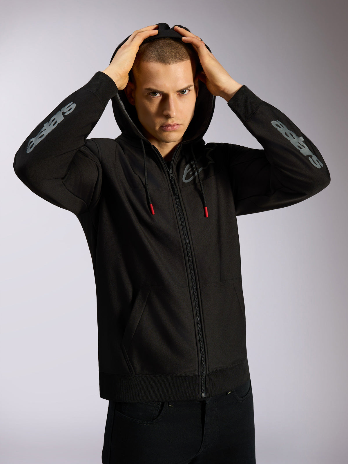 Alpinestars Sessions V3 Hoodie, czarna bluza z kapturem zapinana na zamek, szare logotypy Astars na przedramionach, kaptur z podszewką z siateczki i sznurkami z czerwonymi końcówkami, codzienna odzież typu streetwear inspirowana motorsportem