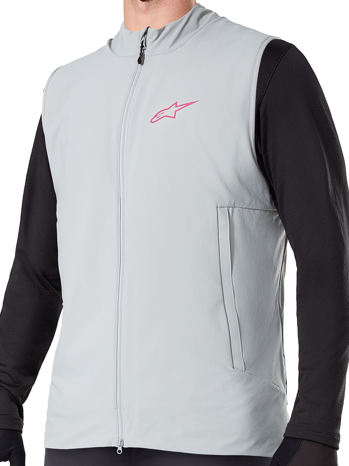 Alpinestars A-Dura Thermal Vest, ocieplana kamizelka rowerowa w kolorze Titanium Gray, różowe logo gwiazdy na piersi, założona na czarną bluzkę z długim rękawem, posiada pionową kieszeń na zamek i pełny zamek z przodu, zaprojektowana do jazdy MTB w chłodne dni.