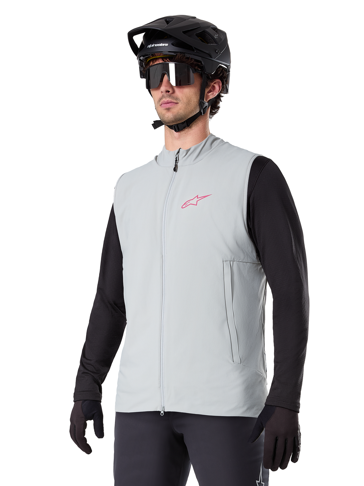 Kamizelka termiczna Alpinestars A-Dura, Titanium Gray, rowerowa kamizelka ocieplana, założona na czarną koszulkę z długim rękawem, z czarnym kaskiem MTB i rękawiczkami, różowe logo na piersi, pionowe boczne kieszenie na zamek
